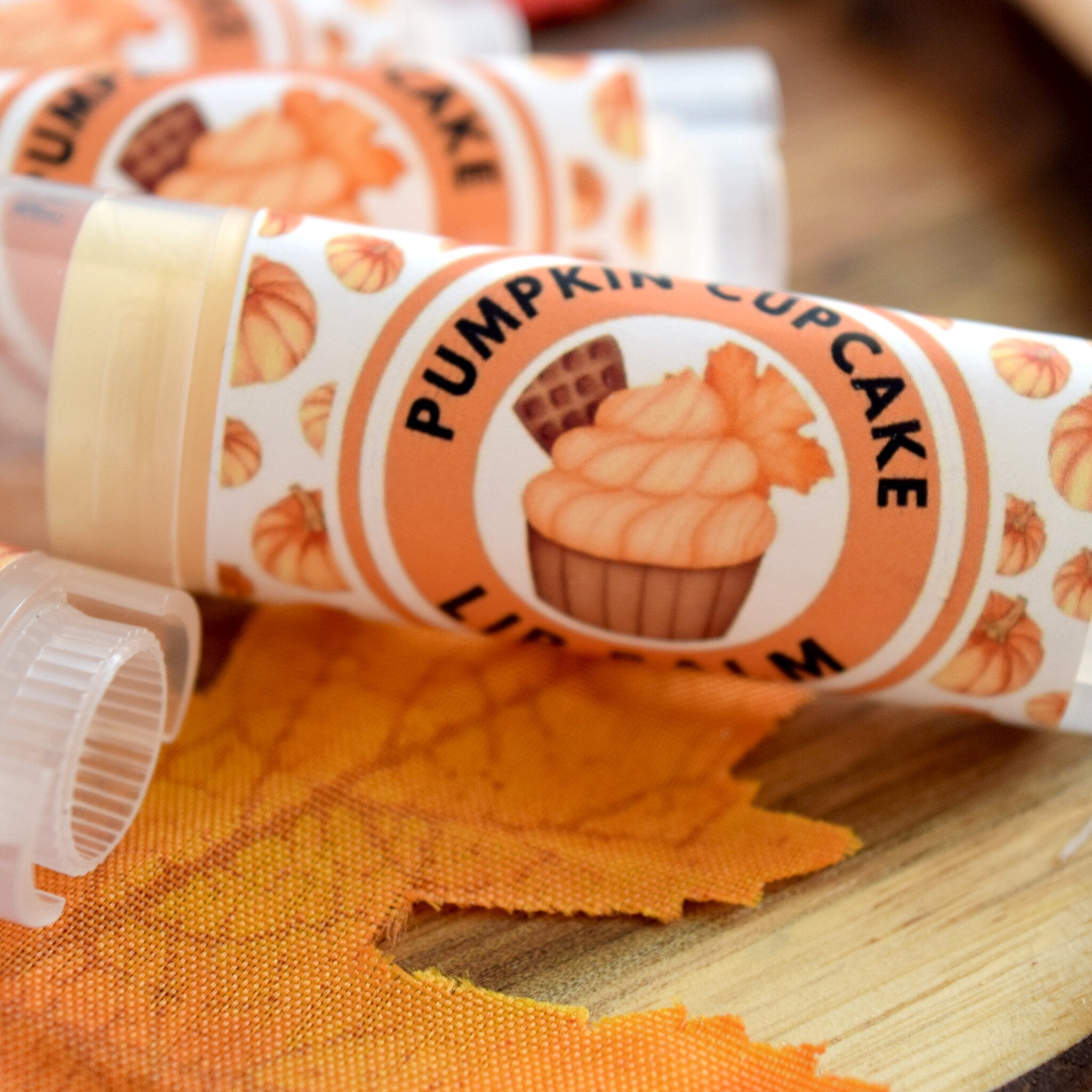 Lip balm tubes with orange and white labels, pumpkin pattern, and "Pumpkin Cupcake" text