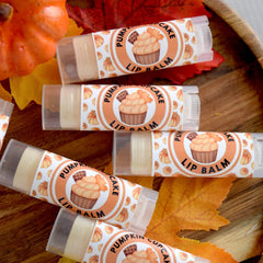 Lip balm tubes with "Pumpkin Cupcake Lip Balm" text, clear plastic, and beige balm inside, on wood surface