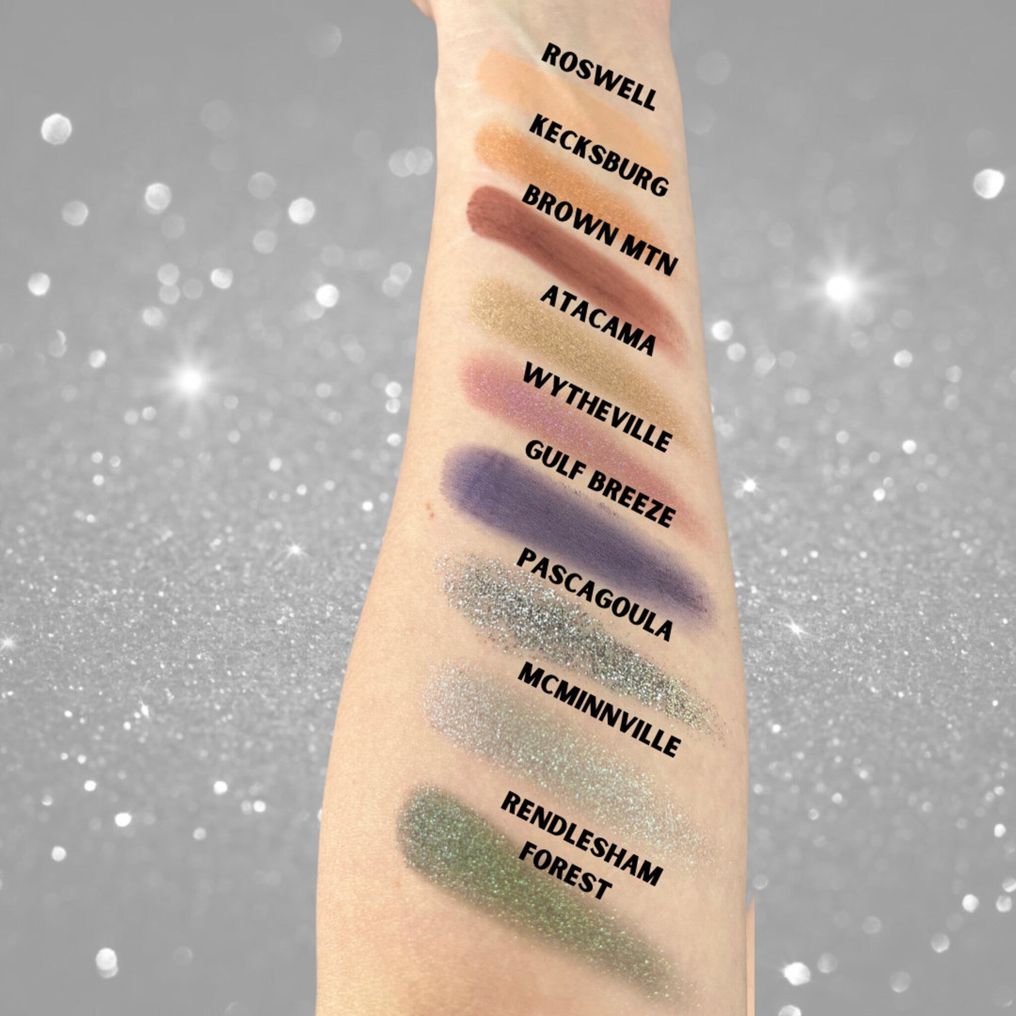 Eyeshadow swatches in various colors on arm, with text labels in black font