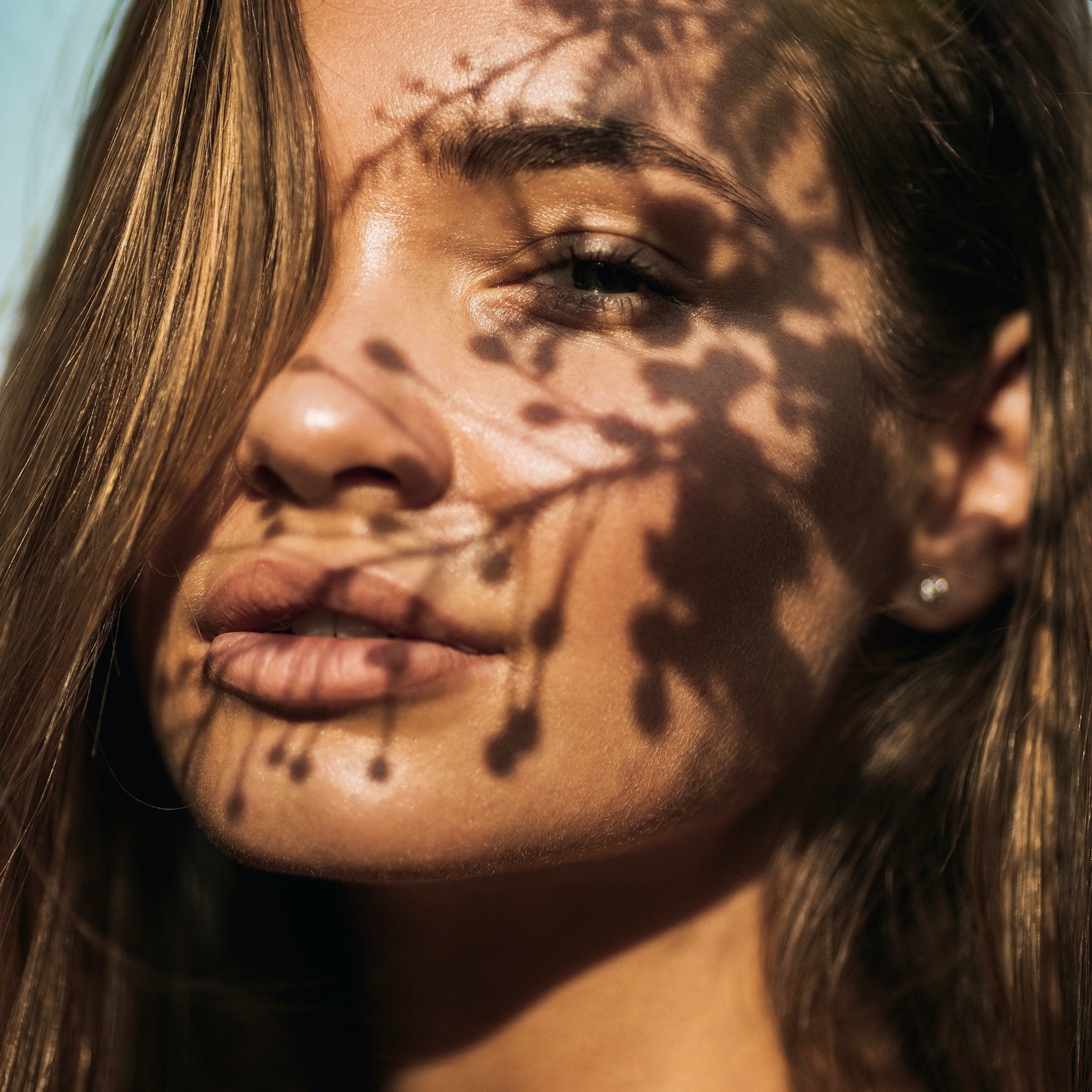 Woman's face with brown hair, shadow pattern, and neutral skin tone in natural light