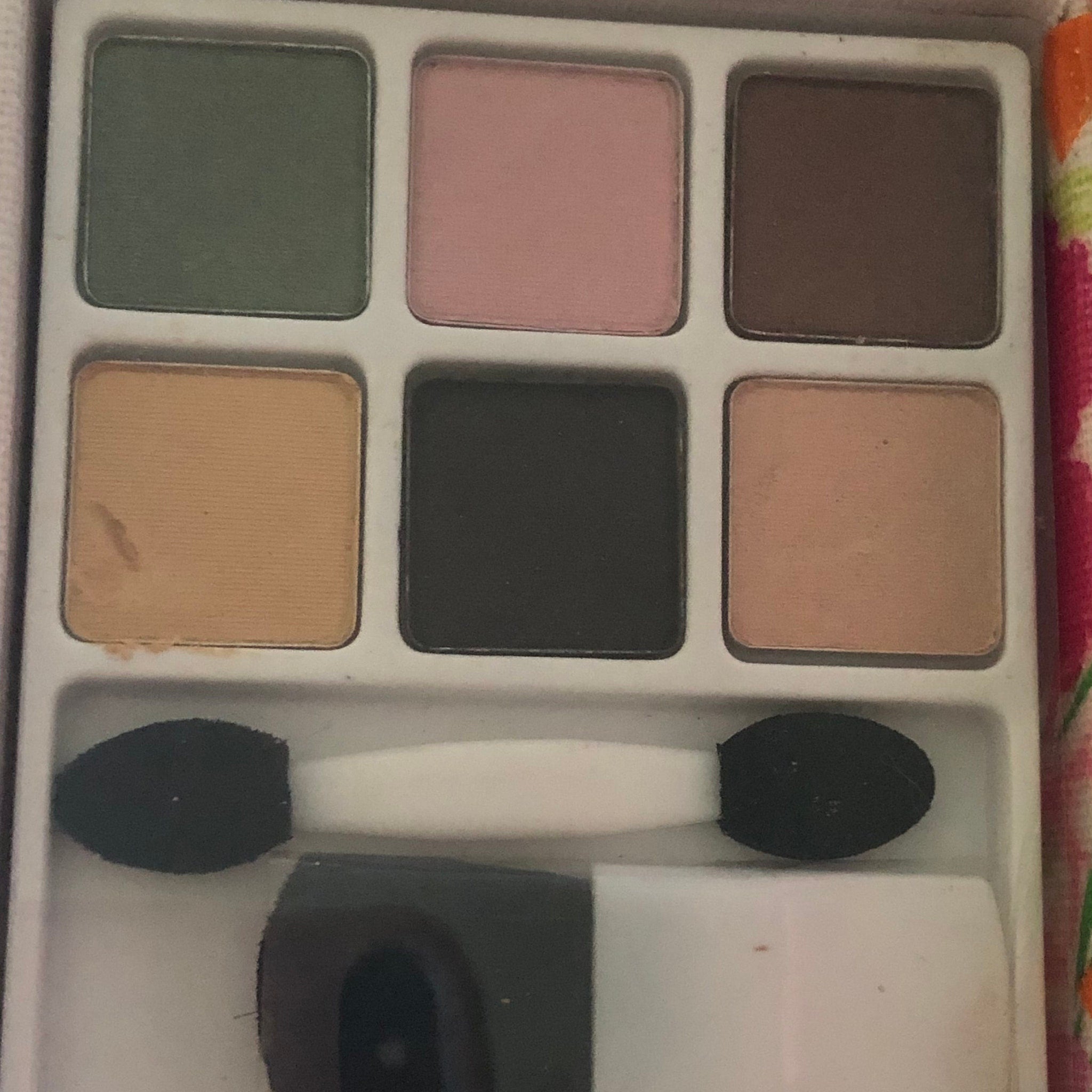 Eyeshadow palette with green, pink, and brown shades, plus applicators, in a compact case