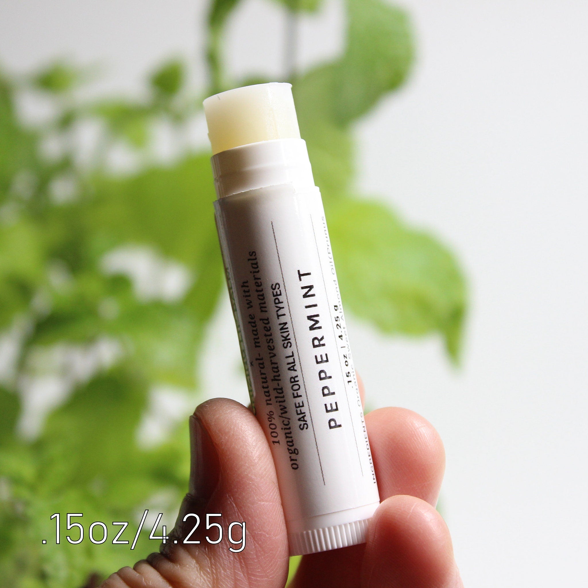 Lip balm stick with white tube, visible Peppermint text, and pale yellow balm tip held in hand