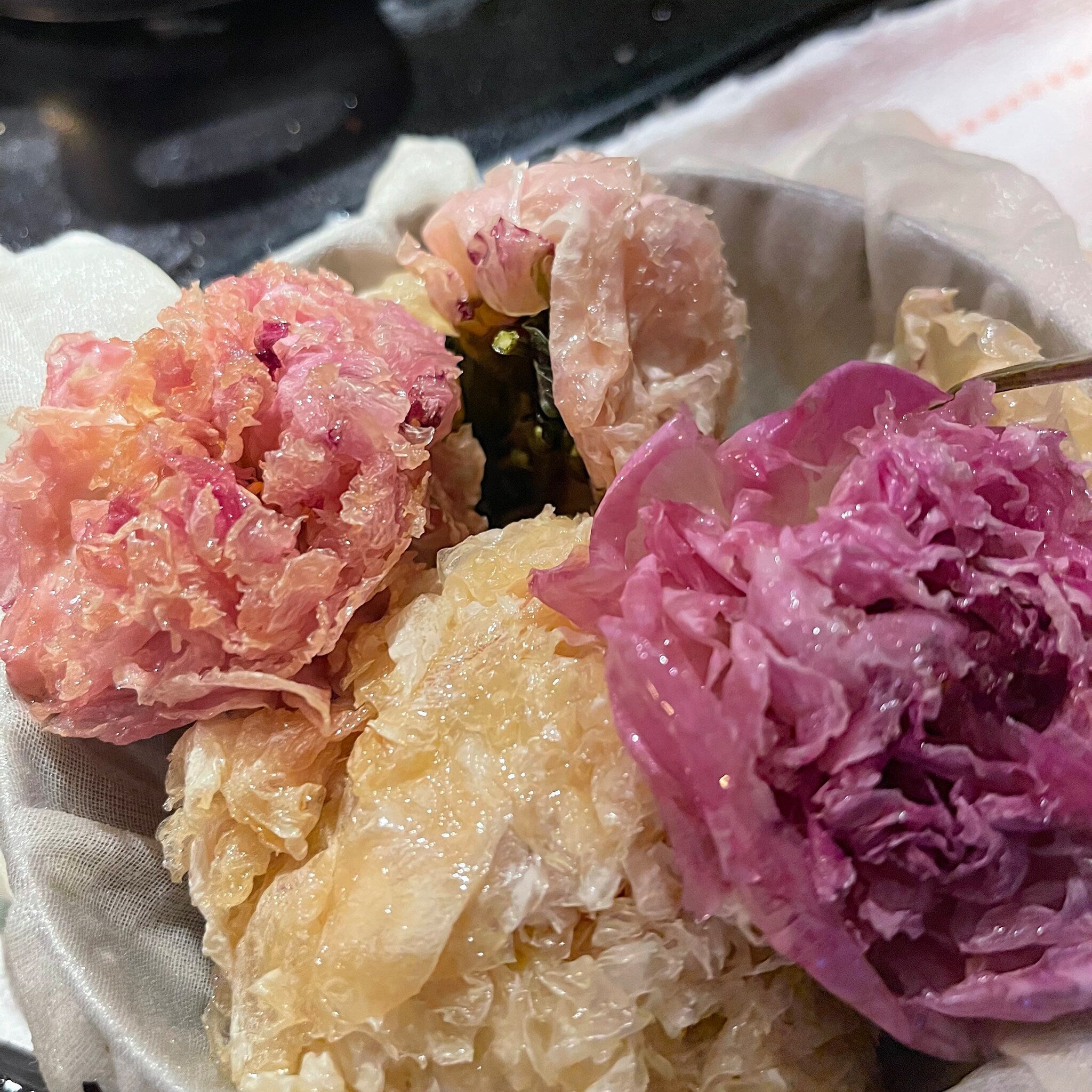 Pink and yellow floral arrangement with crumpled petals in a cloth-lined bowl, close-up view