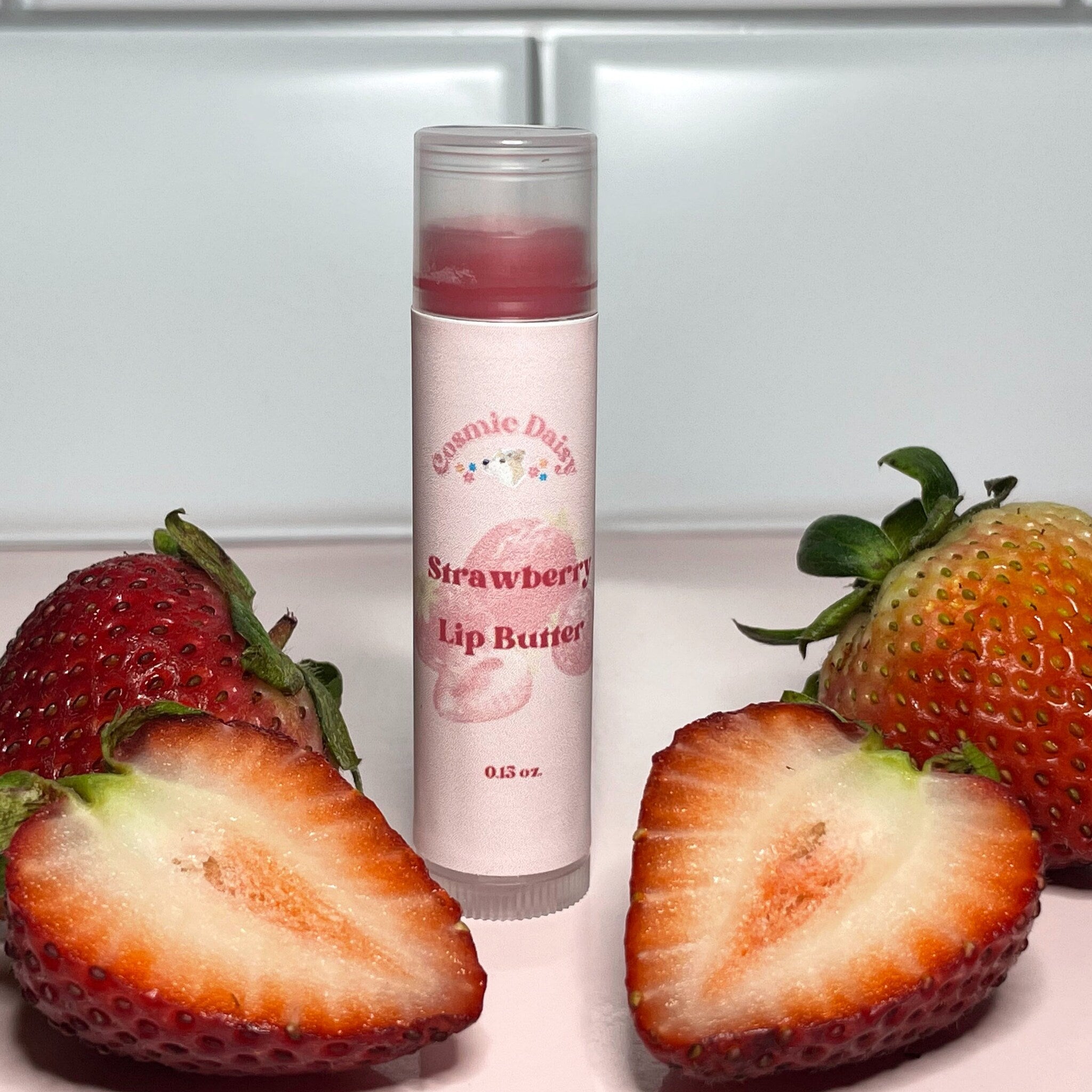 Lip balm tube with pink label, clear cap, and strawberry fruit, Cosmic Daisy brand