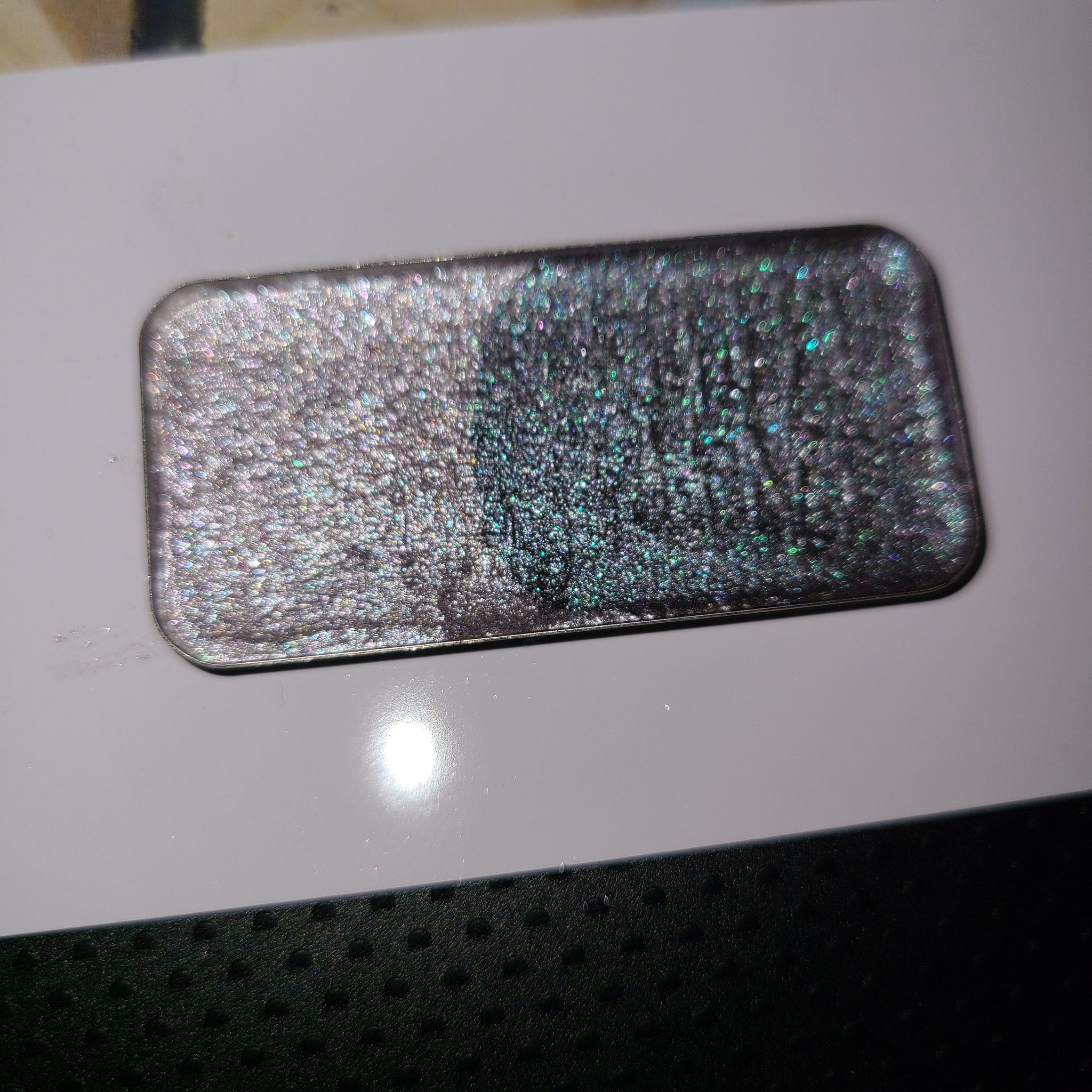 Square compact with mirrored lid showcasing multichrome eyeshadow in shifting blue-purple hues.