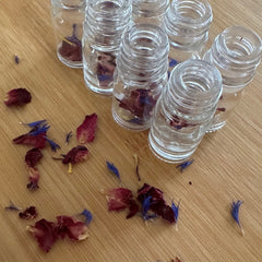 Glass bottles with clear material, red and blue petals, on wood surface