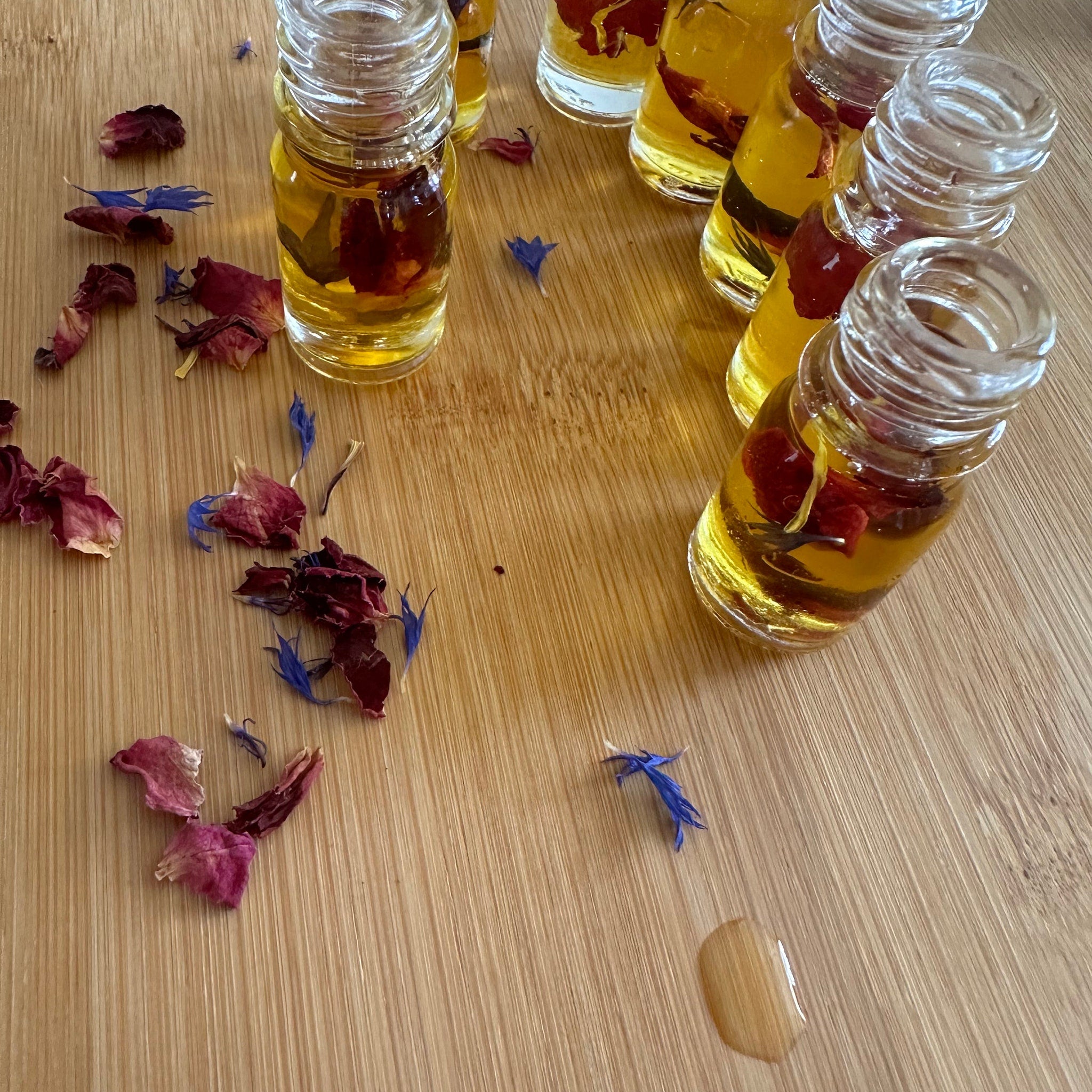 Small glass bottles with yellow liquid, red petals, and blue flowers on wood surface