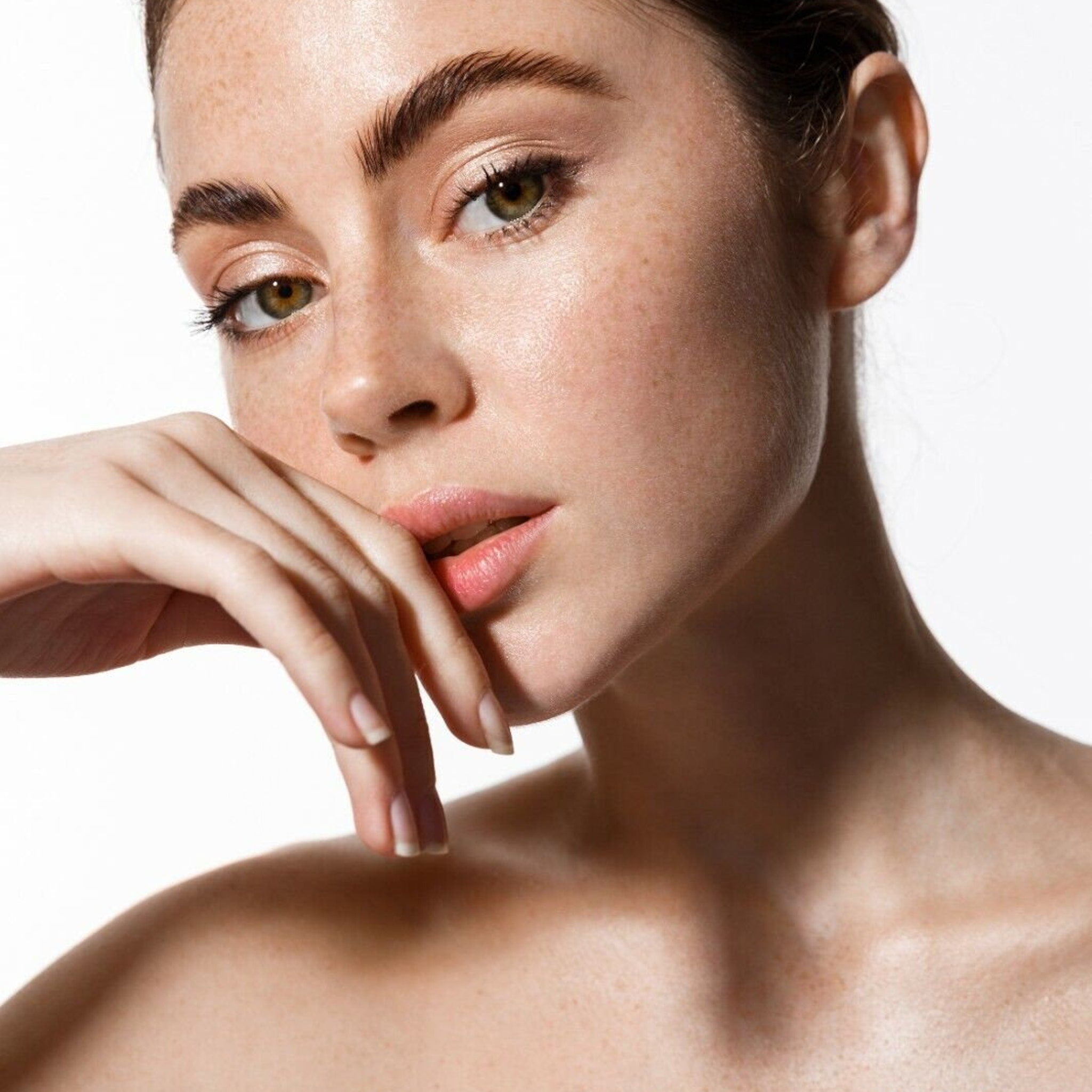 Woman's face with light skin, hand near mouth, and light eye makeup, looking at camera