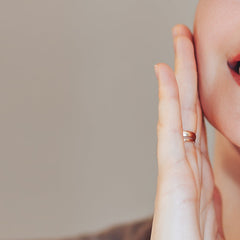 Hand with gold ring, touching face, with red lipstick and neutral background