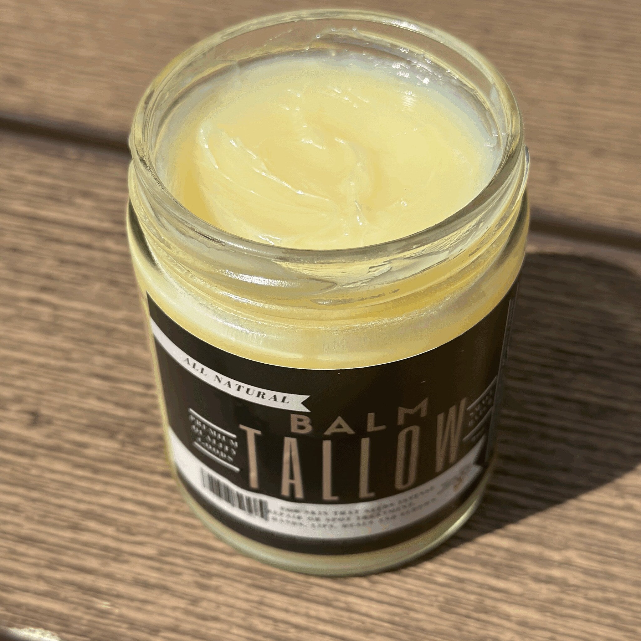 Tallow balm jar with pale yellow color, glass container, and black label with text on wood surface