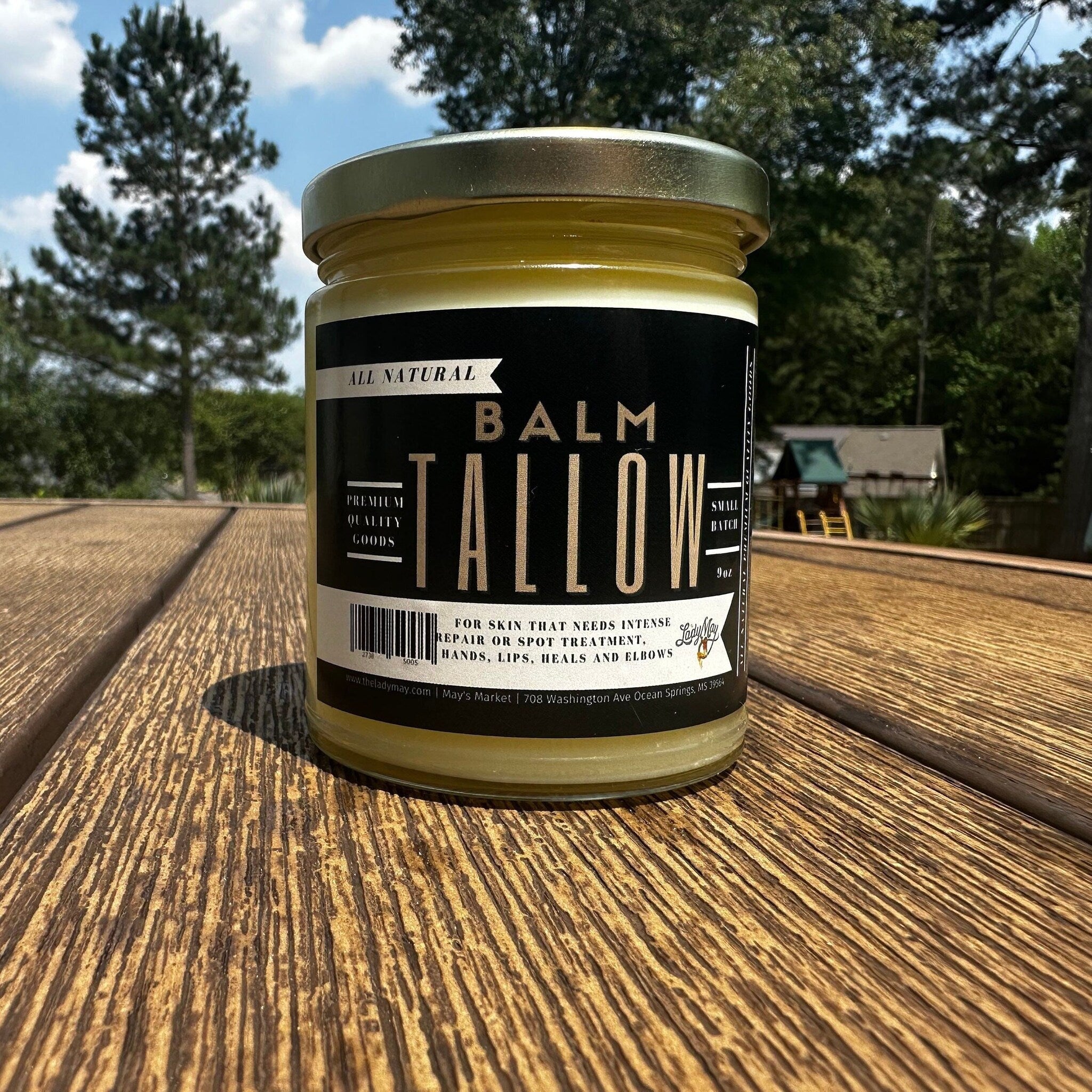 Tallow balm in a glass jar with black label, yellow contents, and Lady May brand text on wooden table