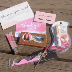 Eyelash kit with pink applicator, clear adhesive, and thank you cards on wood surface