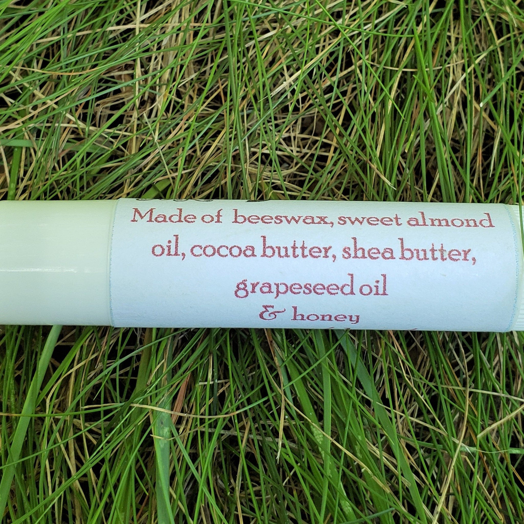 Lip balm tube with white and pink text on a green background of grass