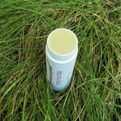 Lip balm tube, white with green text, light yellow balm, in green grass