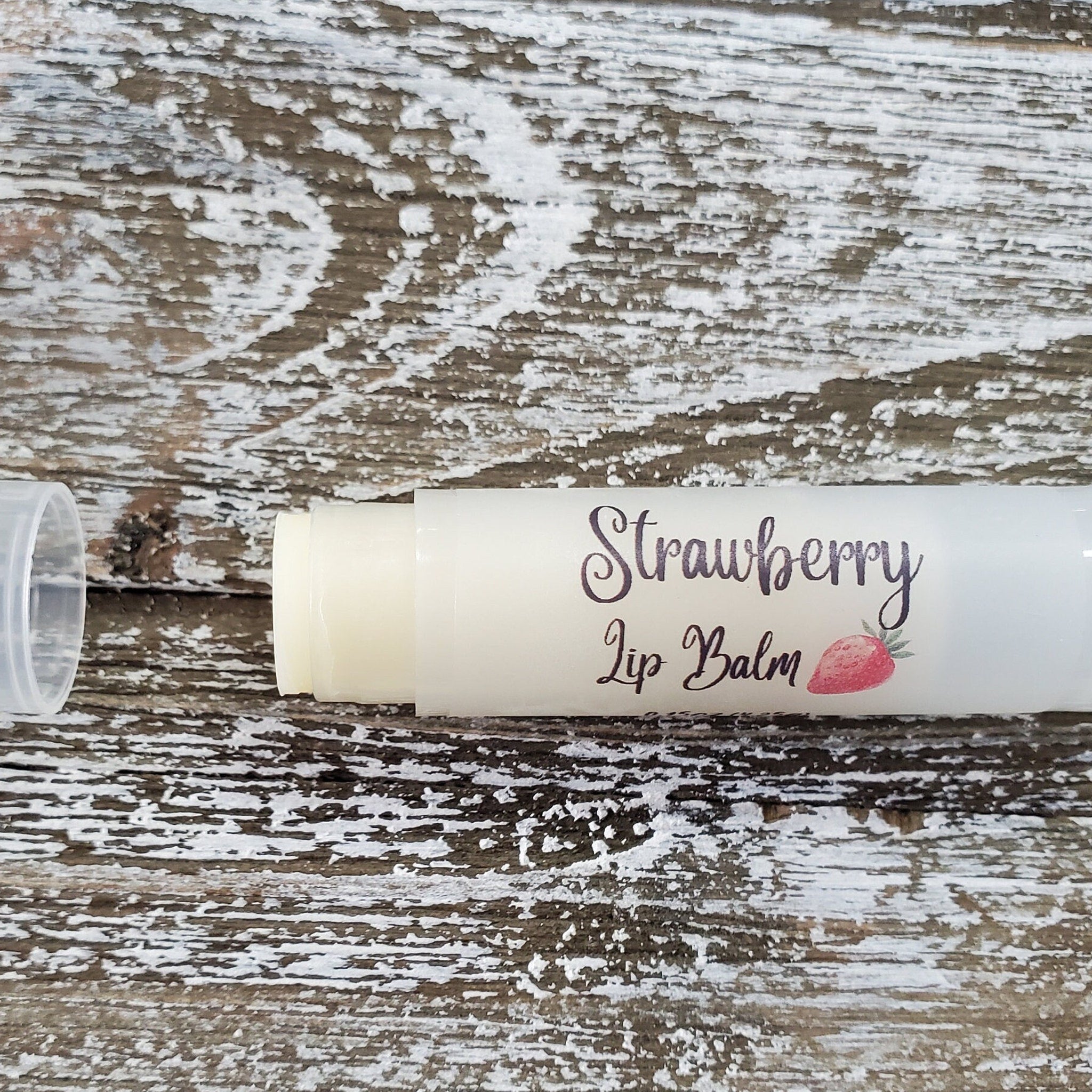 Strawberry lip balm in white tube with label, on wood background, Griffin Lily Designs text visible