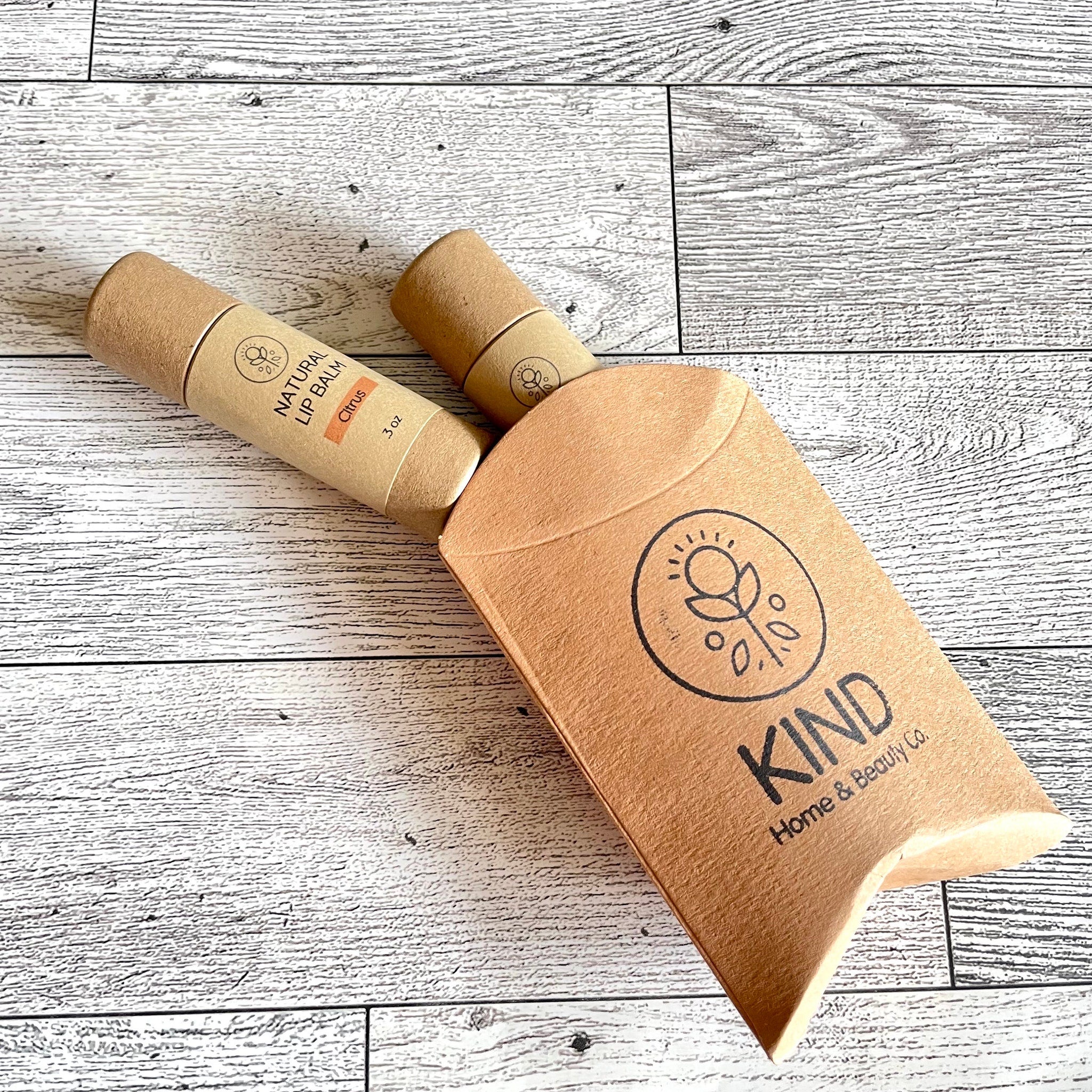 Lip balm tubes with brown paper packaging and KIND branding on a wooden surface
