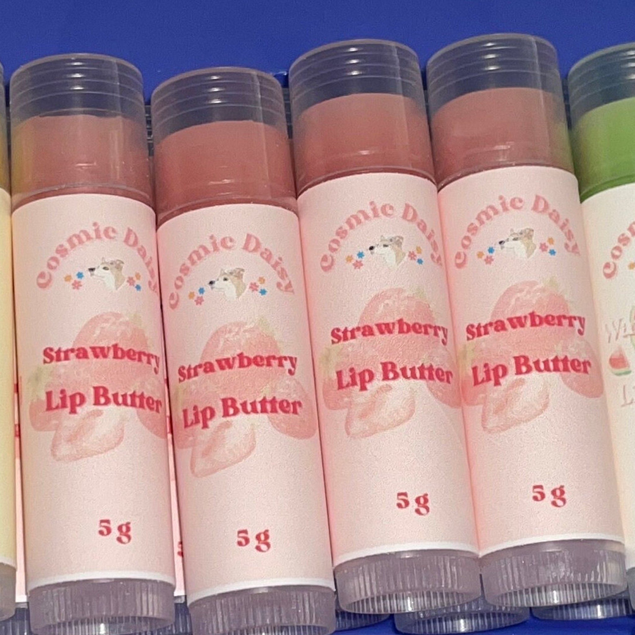 Strawberry lip butter tubes, pink label with strawberry graphic, clear plastic top, Cosmic Daisy brand