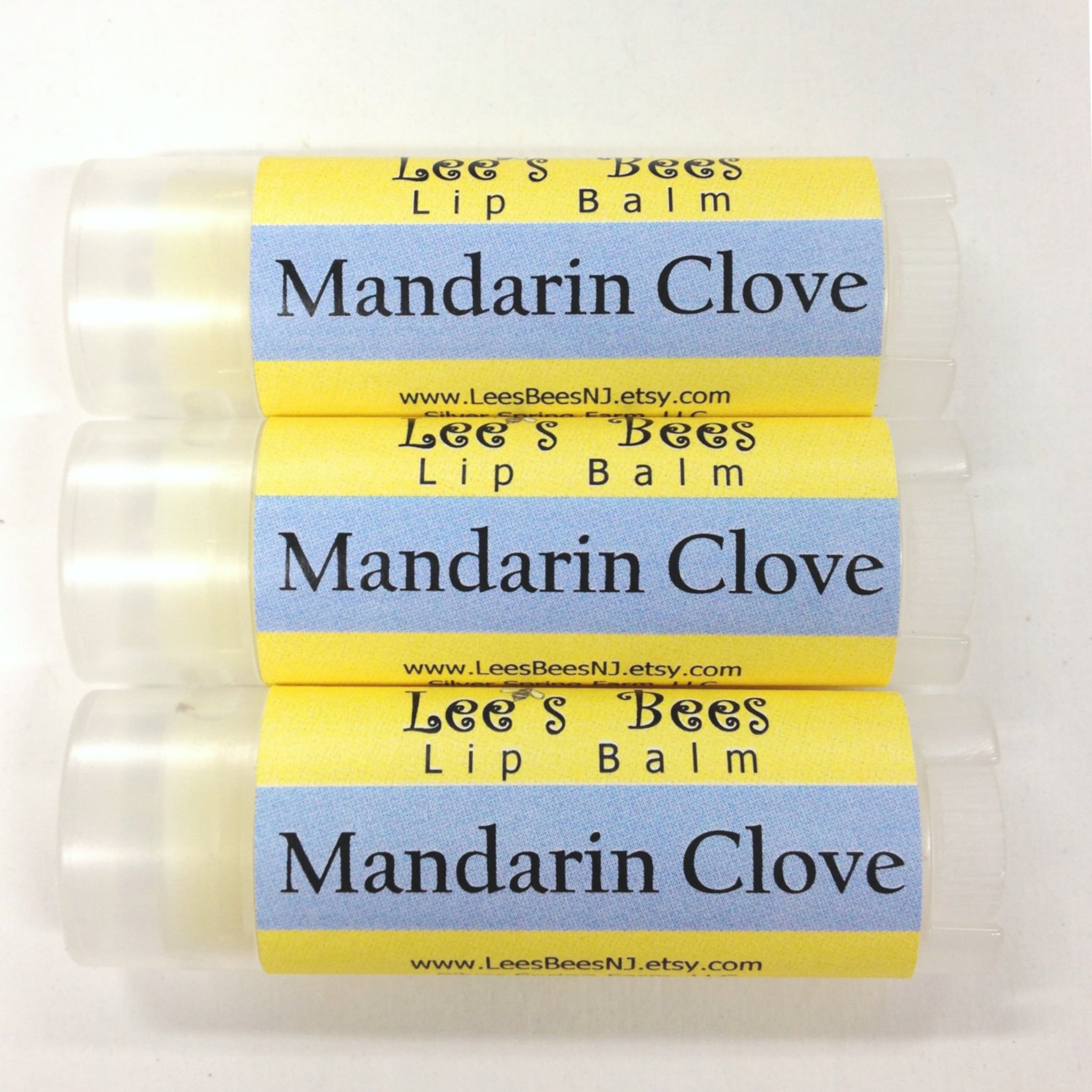 Lip balm tubes with yellow and blue labels, "Lee's Bees" brand, "Mandarin Clove" text, clear tubes