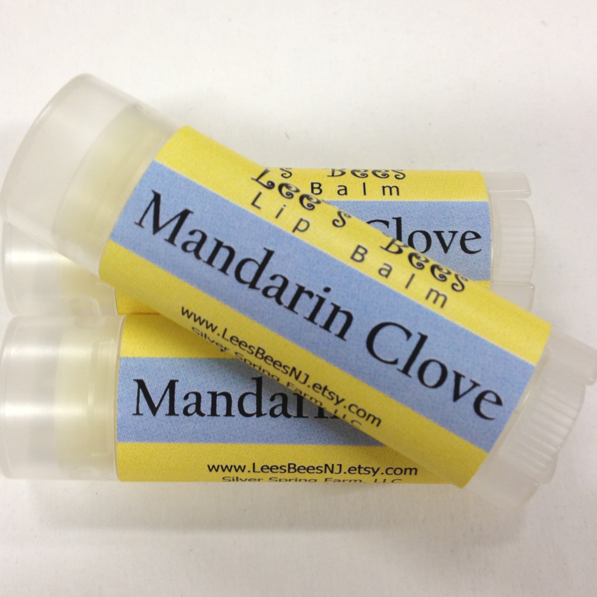 Lip balm with yellow and blue label, clear plastic tube, and "Mandarin Clove" text