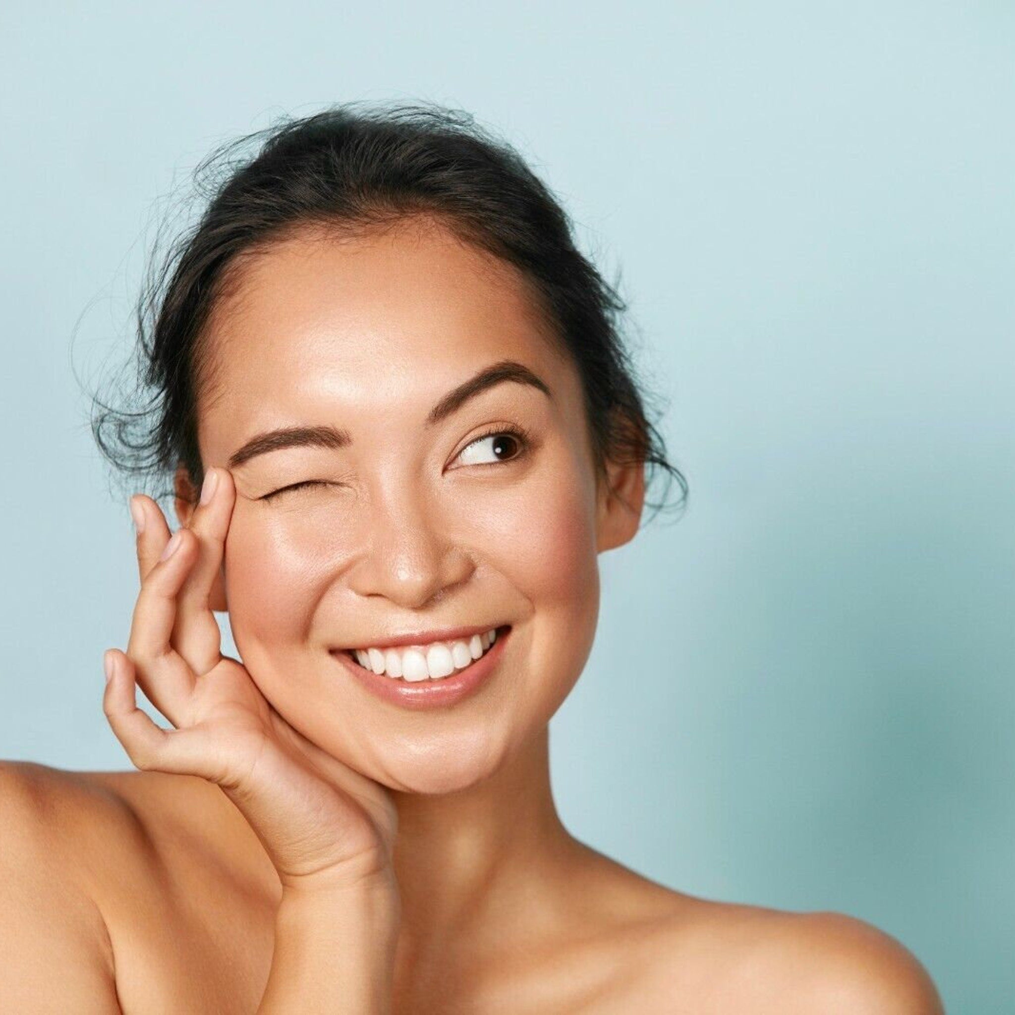 Woman winking with dark hair, fair skin, and blue background