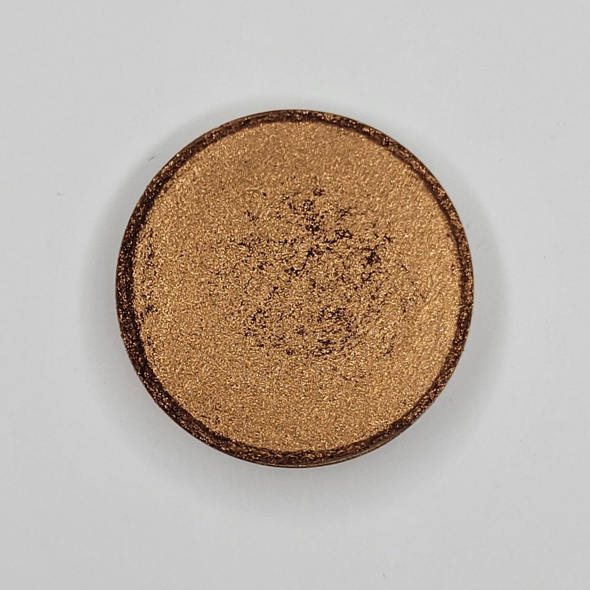 Close-up of Cinnamon Roll Bronze Shimmer Eyeshadow in round compact with warm bronze sparkle and smooth satin finish