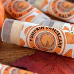 Lip balm tubes with orange and white labels, pumpkin pattern, and "Pumpkin Cheesecake" text visible