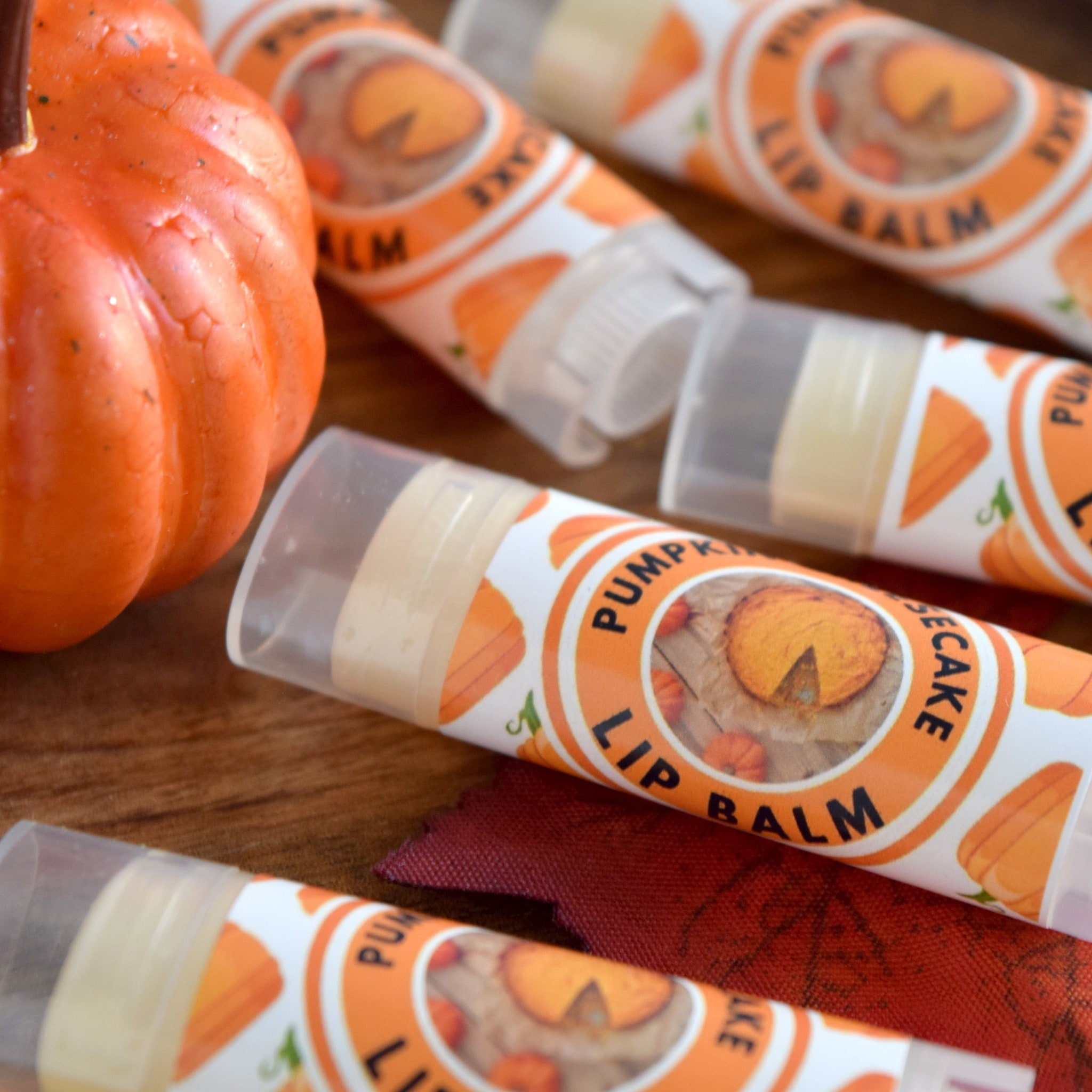 Lip balm tubes with orange and white labels, pumpkin graphic, and clear plastic casing on wood surface