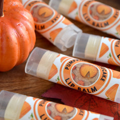 Lip balm tubes with orange and white labels, pumpkin graphic, and clear plastic casing on wood surface