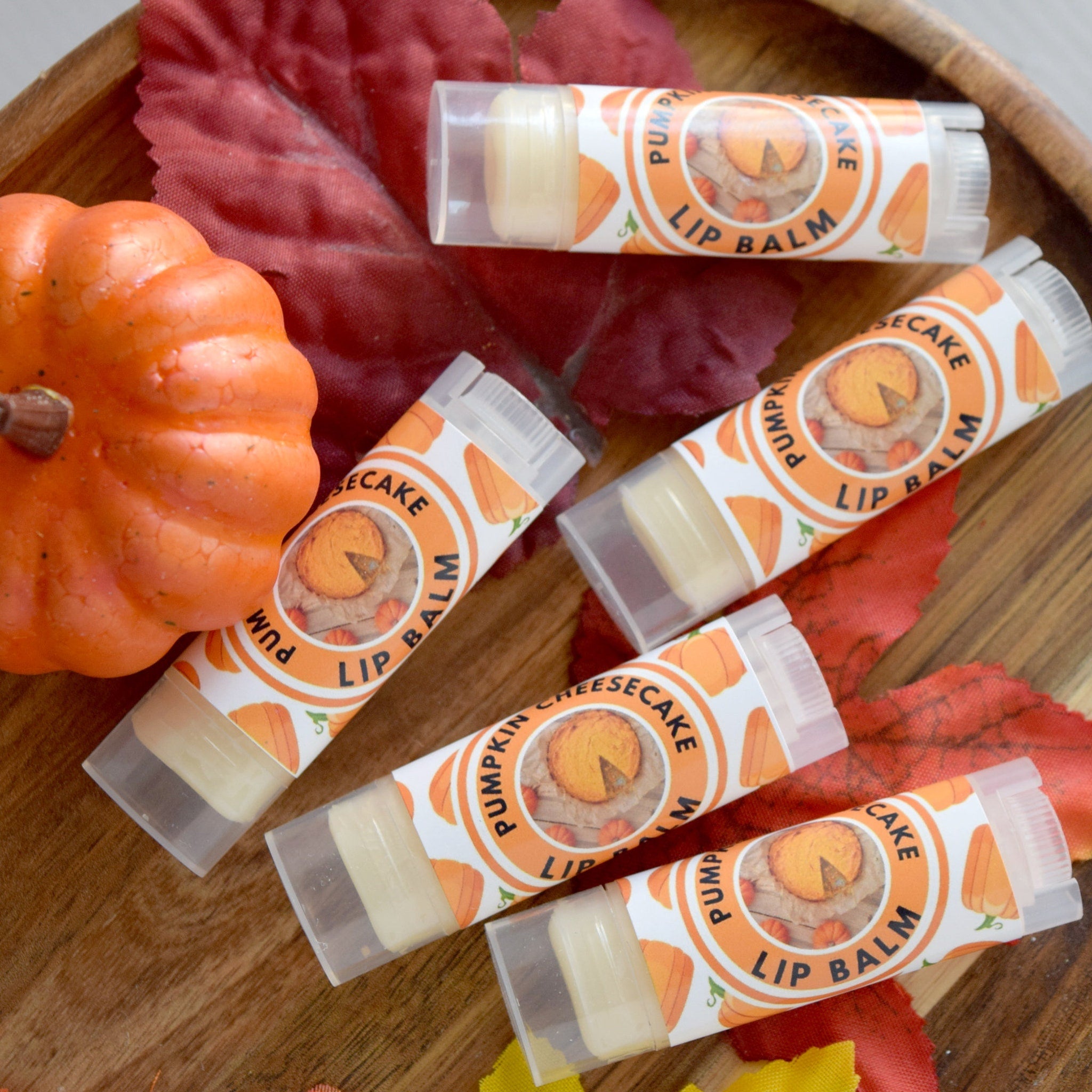 Lip balm tubes with orange and white labels, clear plastic tubes, and pumpkin design on wooden surface