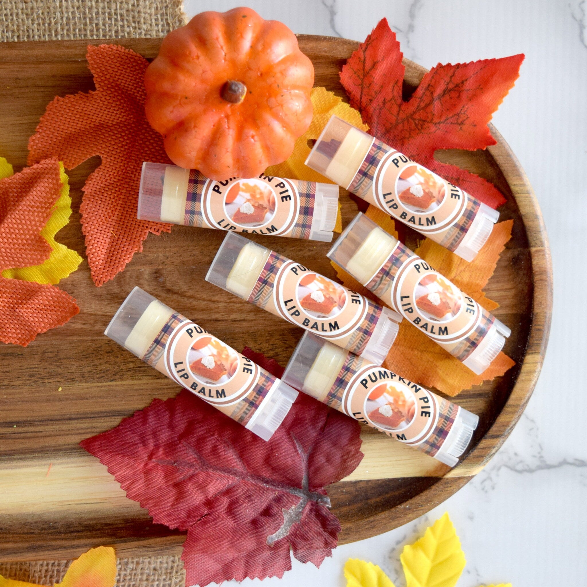 Lip balm tubes with plaid pattern and "Pumpkin Pie" label, on wood tray with fall leaves