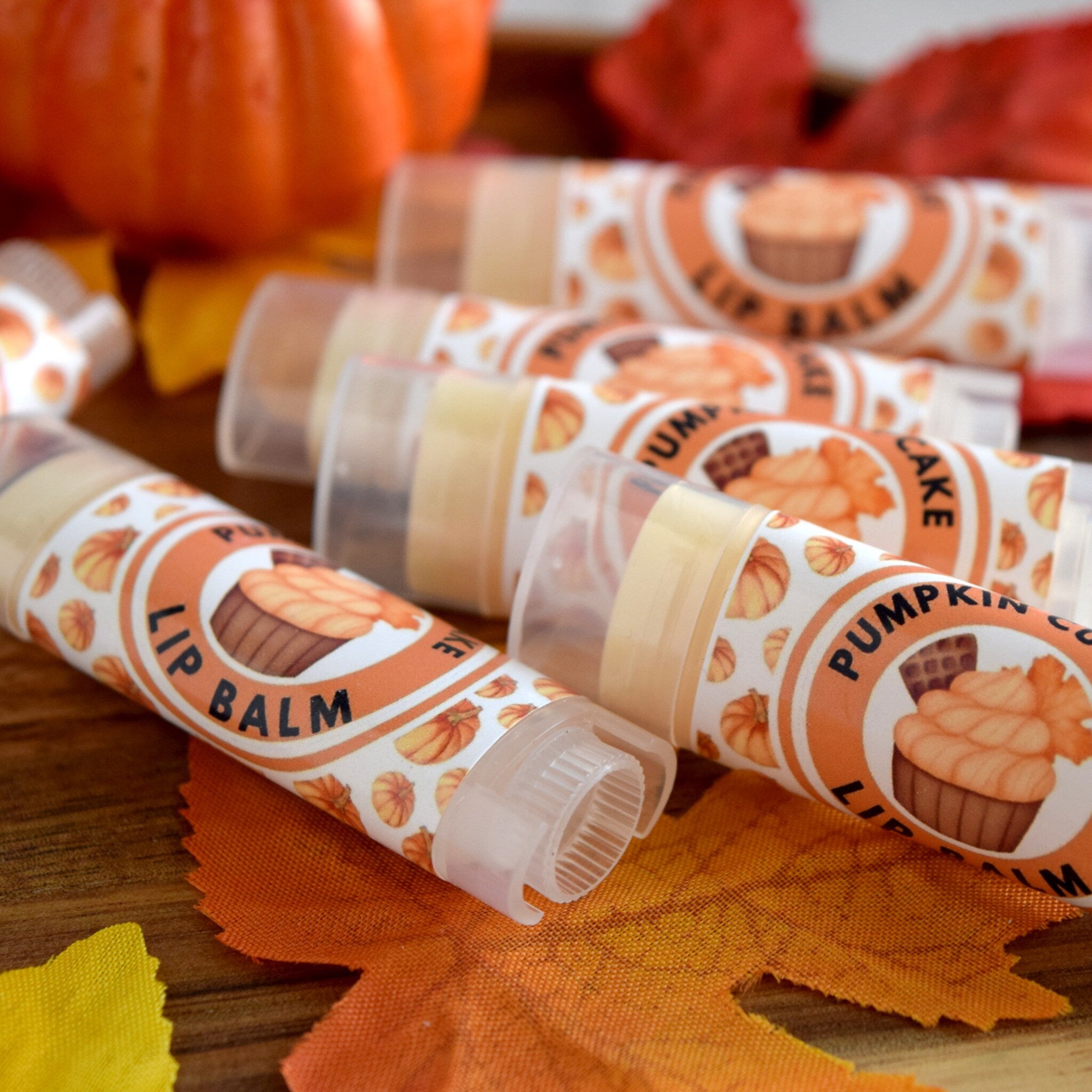 Lip balm tubes with orange and white labels, pumpkin pattern, and clear plastic packaging