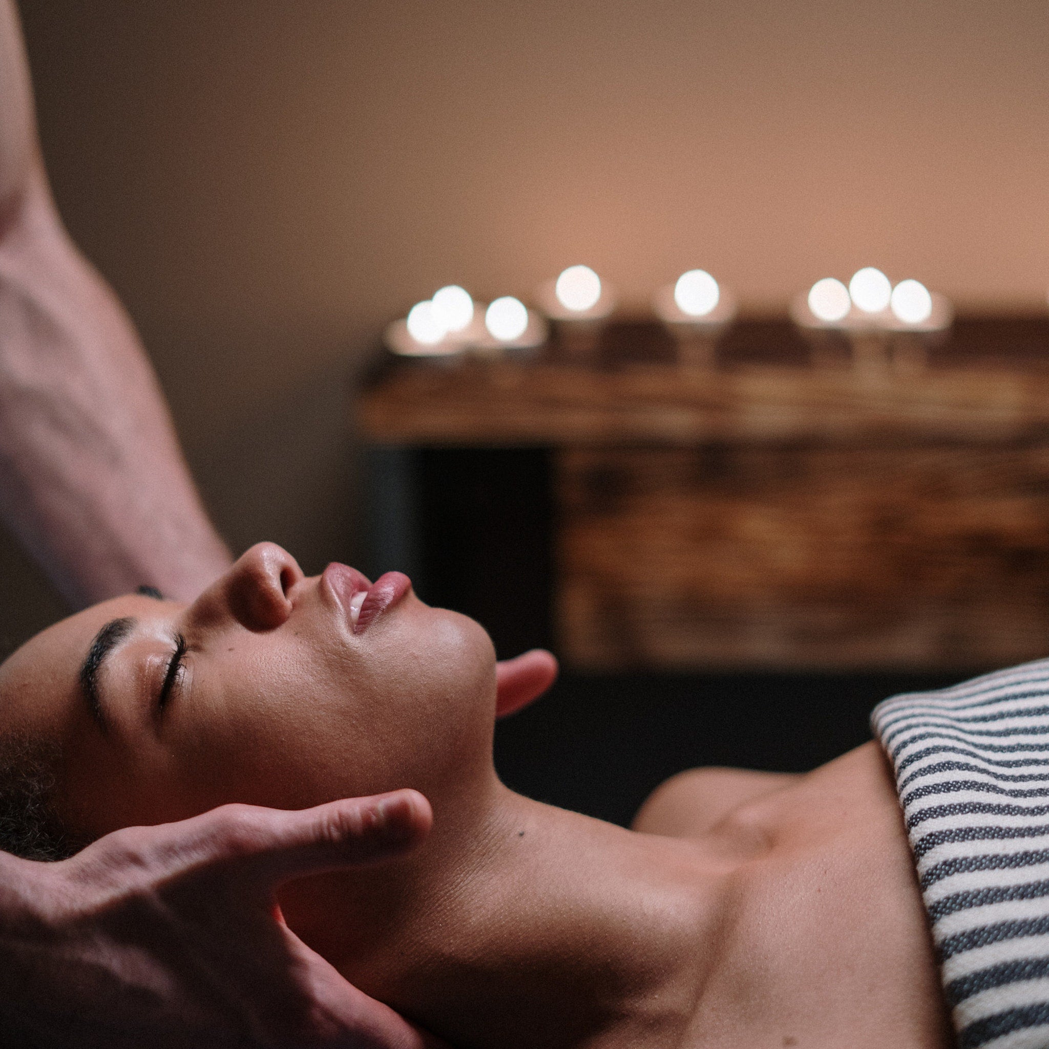 Massage therapy session with person receiving neck massage, striped towel, and blurred lights in background