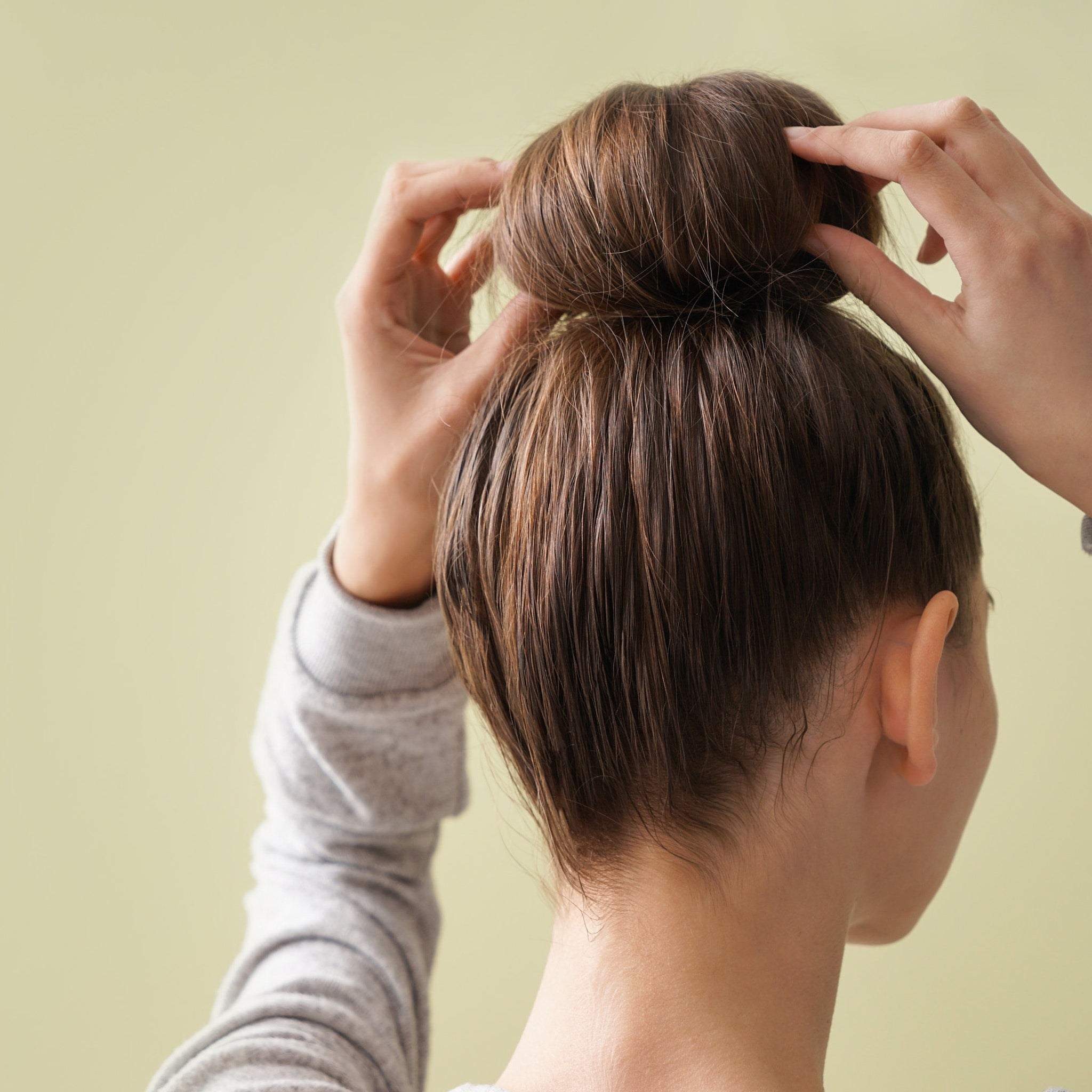 Hair bun style with brown hair being styled by hands, wearing gray shirt