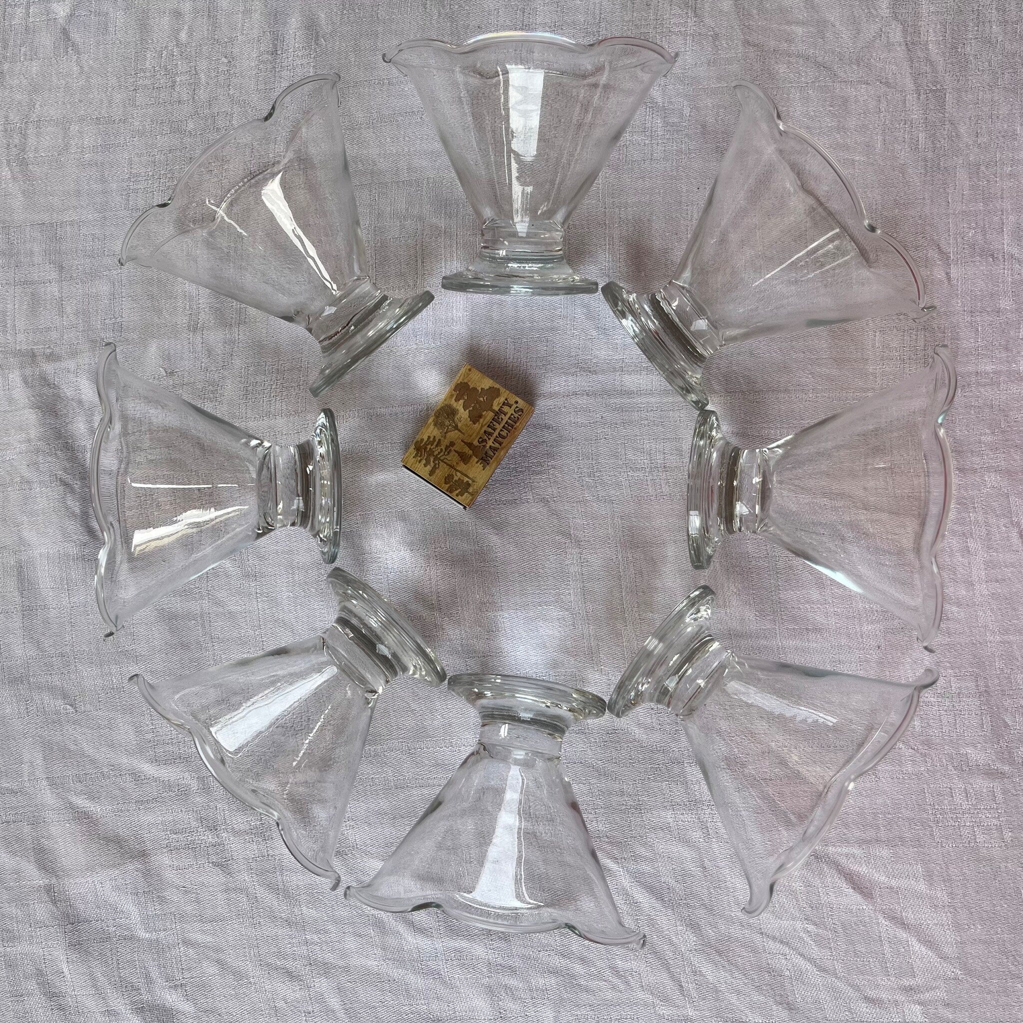 Clear glass dessert dishes with scalloped rims arranged in a circle on a white cloth