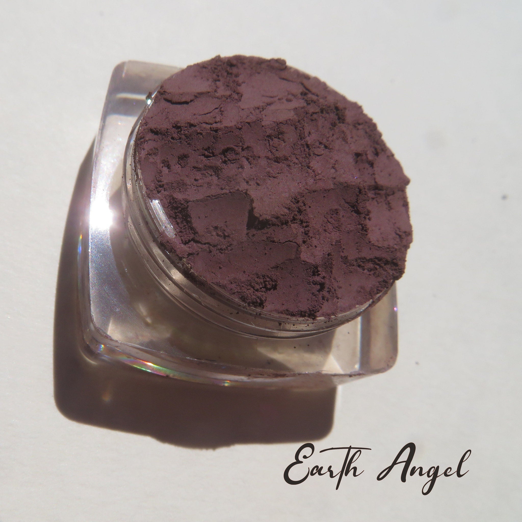 Side view of loose dark purple mineral eyeshadow powder spilling from container with matte finish