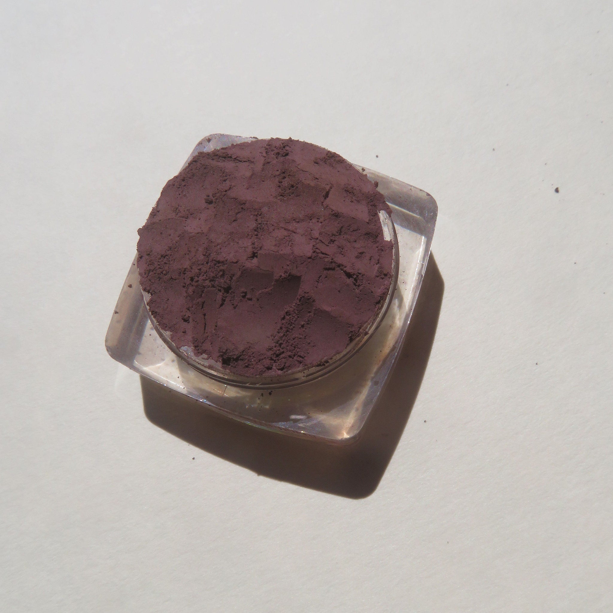 Side view of loose dark purple mineral eyeshadow powder in open jar with angled lighting