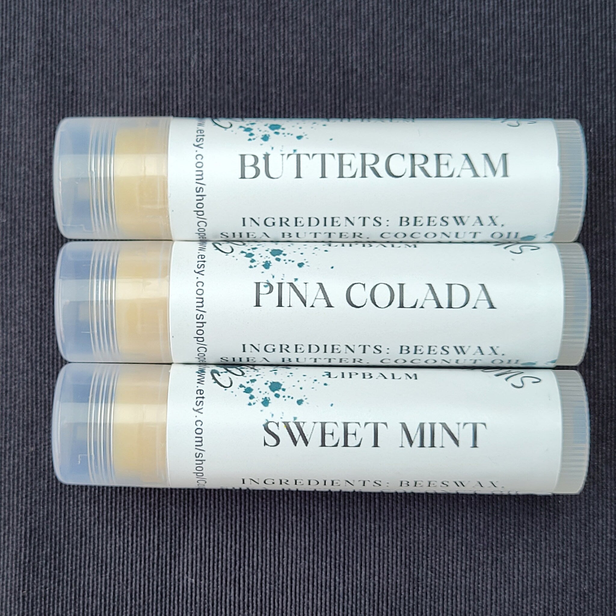 Lip balm tubes with white labels, clear caps, and flavor names visible on a dark background
