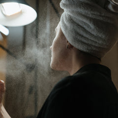 Person wearing white towel, black shirt, and water spray in front of face