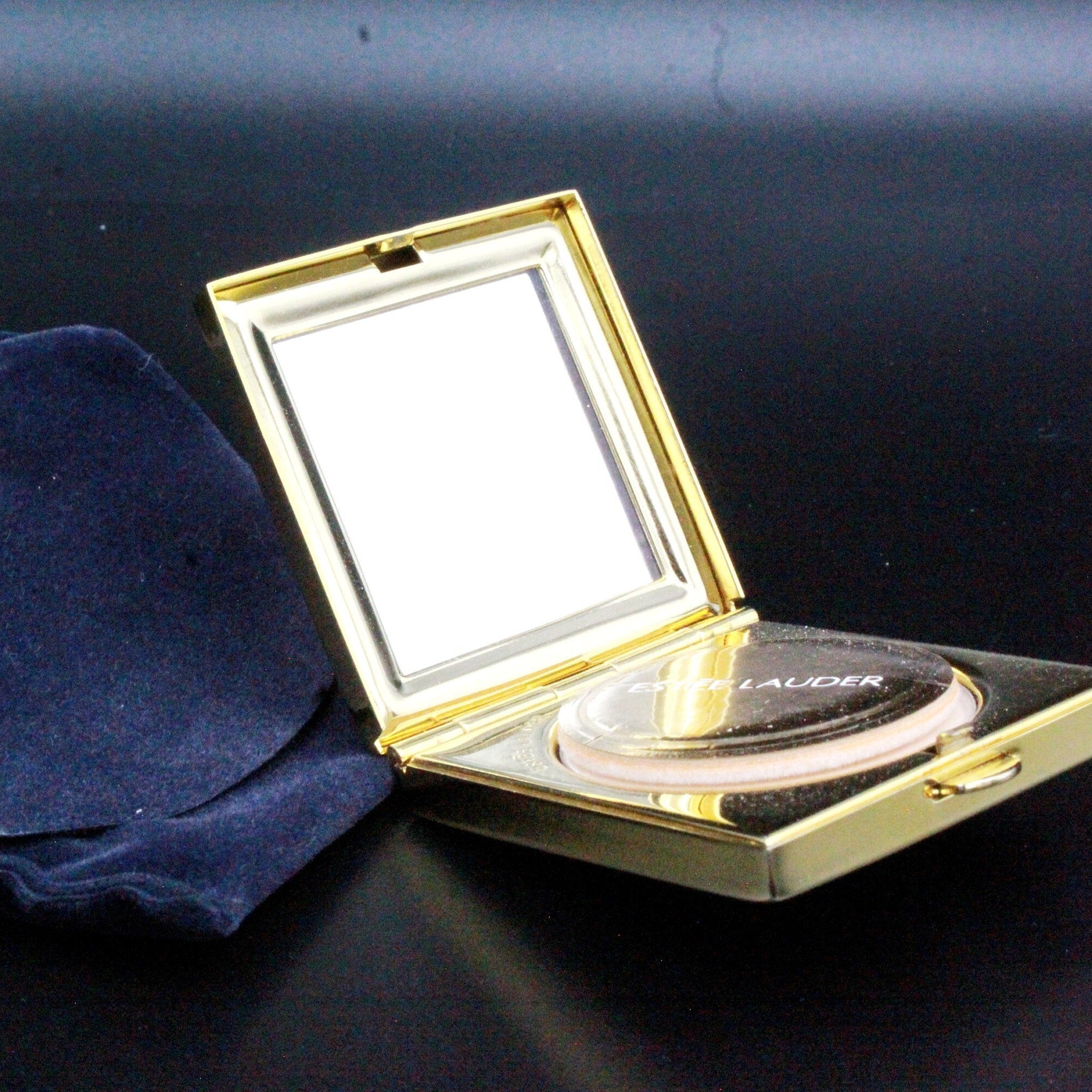 Makeup compact with gold metal case, mirror, and Estee Lauder text visible