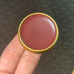 Lip balm in a round gold metal container with red balm, held in hand
