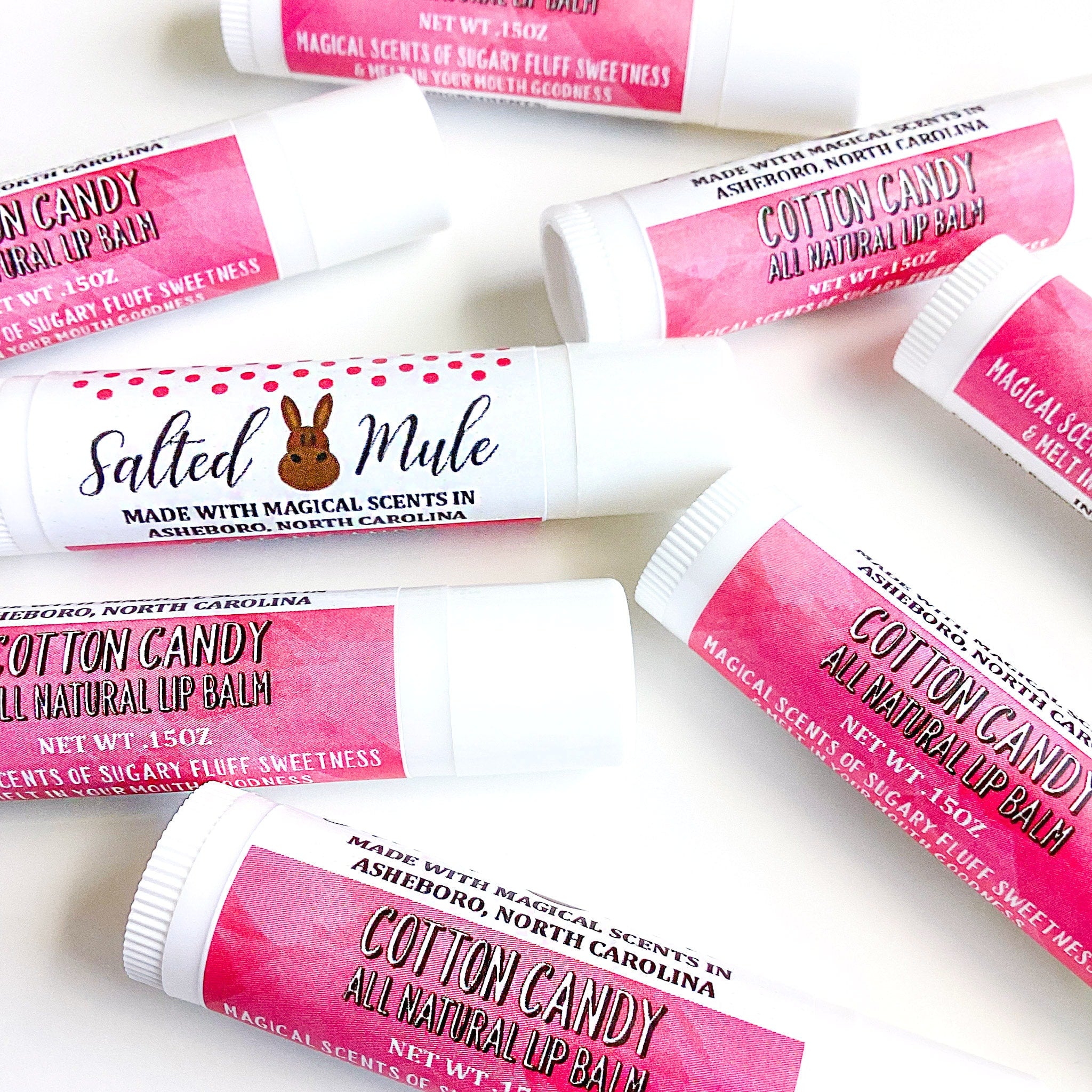 Lip balm tubes with white and pink labels, various text and patterns visible, scattered on white surface