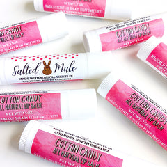 Lip balm tubes with white and pink labels, various text and patterns visible, scattered on white surface