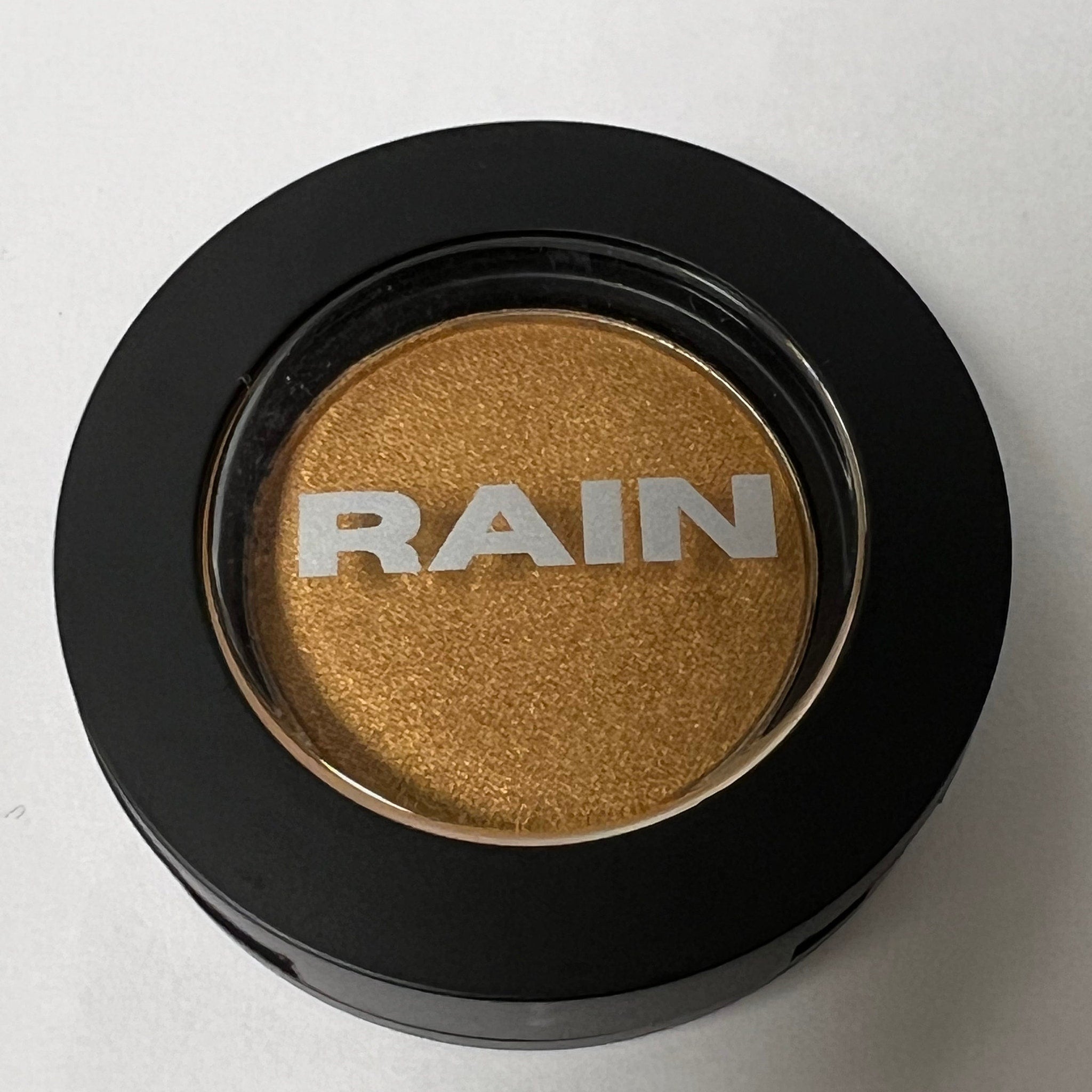 Close-up of sparkling gold pressed powder eye shadow in a sleek black compact with gold trim
