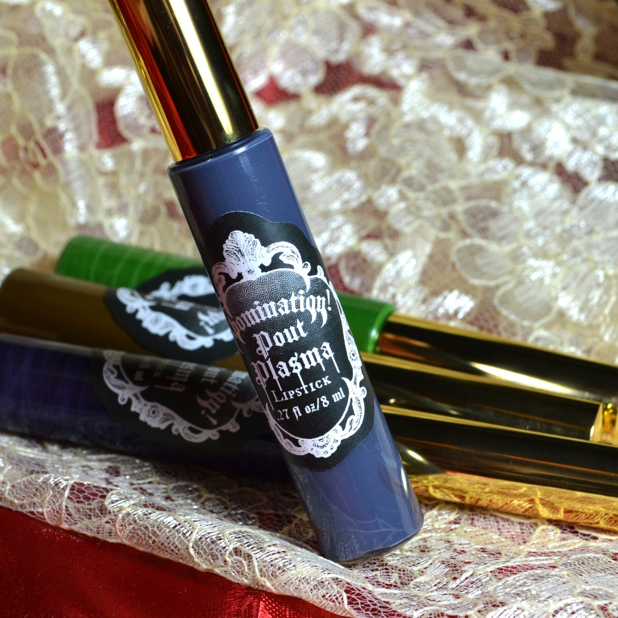 Lipstick tubes in blue, gold, and green with "Domination Pout Plasma" label on lace fabric