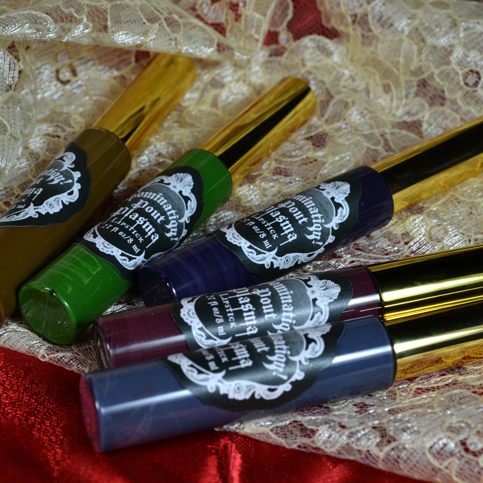 Lipstick tubes with gold caps, various colors, and "pout plasma" label on lace fabric