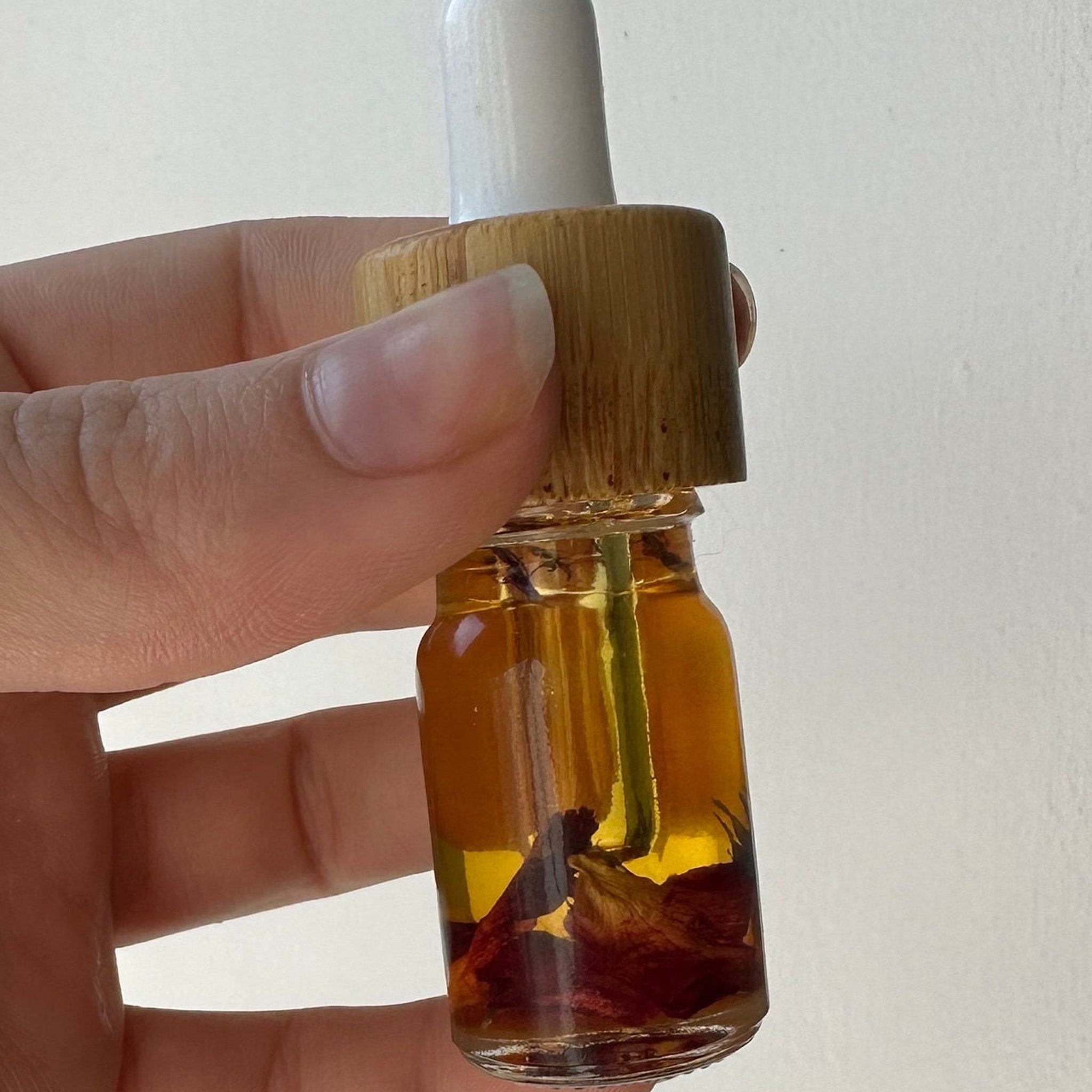 Essential oil bottle with amber liquid, bamboo cap, and white dropper held in hand