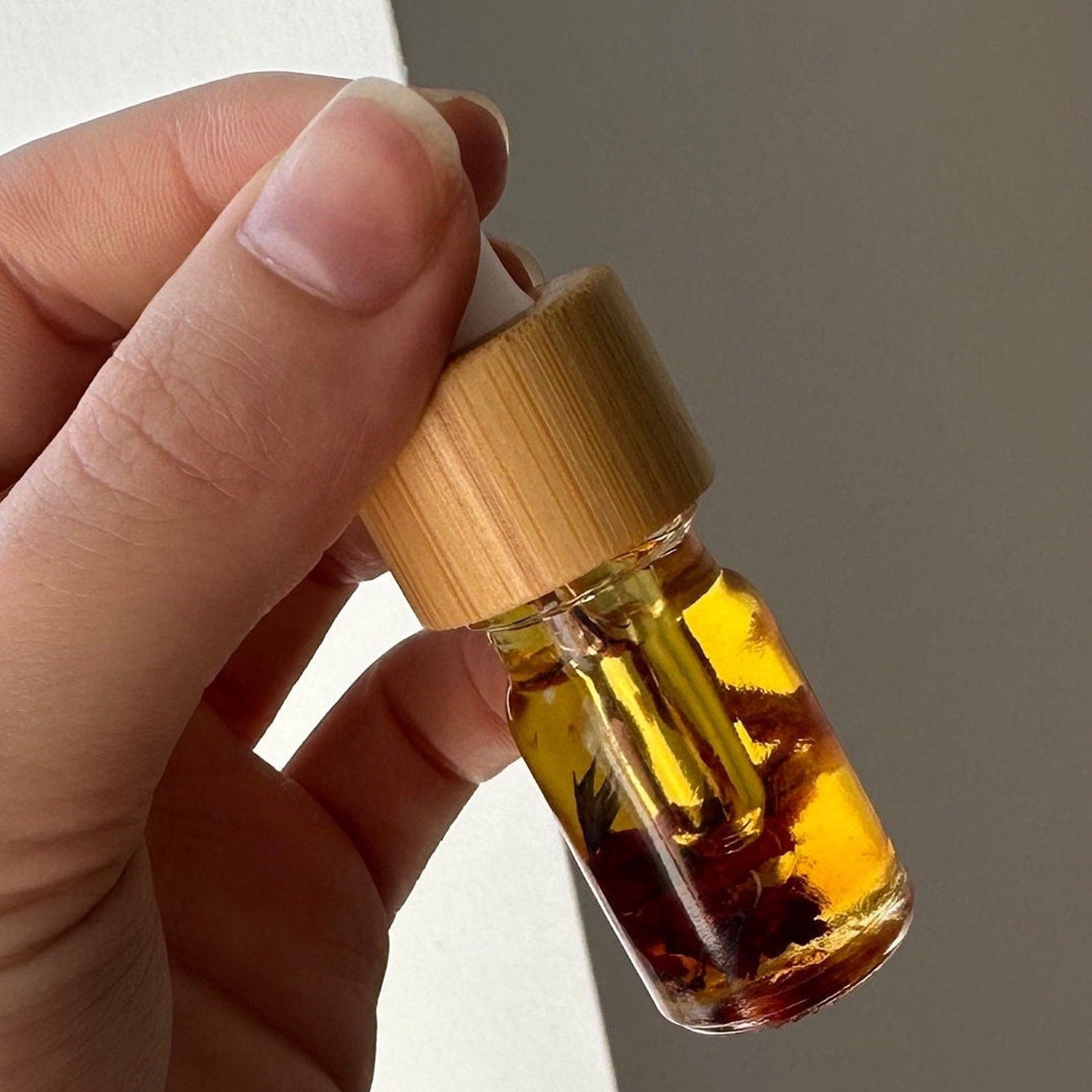 Essential oil bottle with yellow liquid, wooden cap, and held by hand