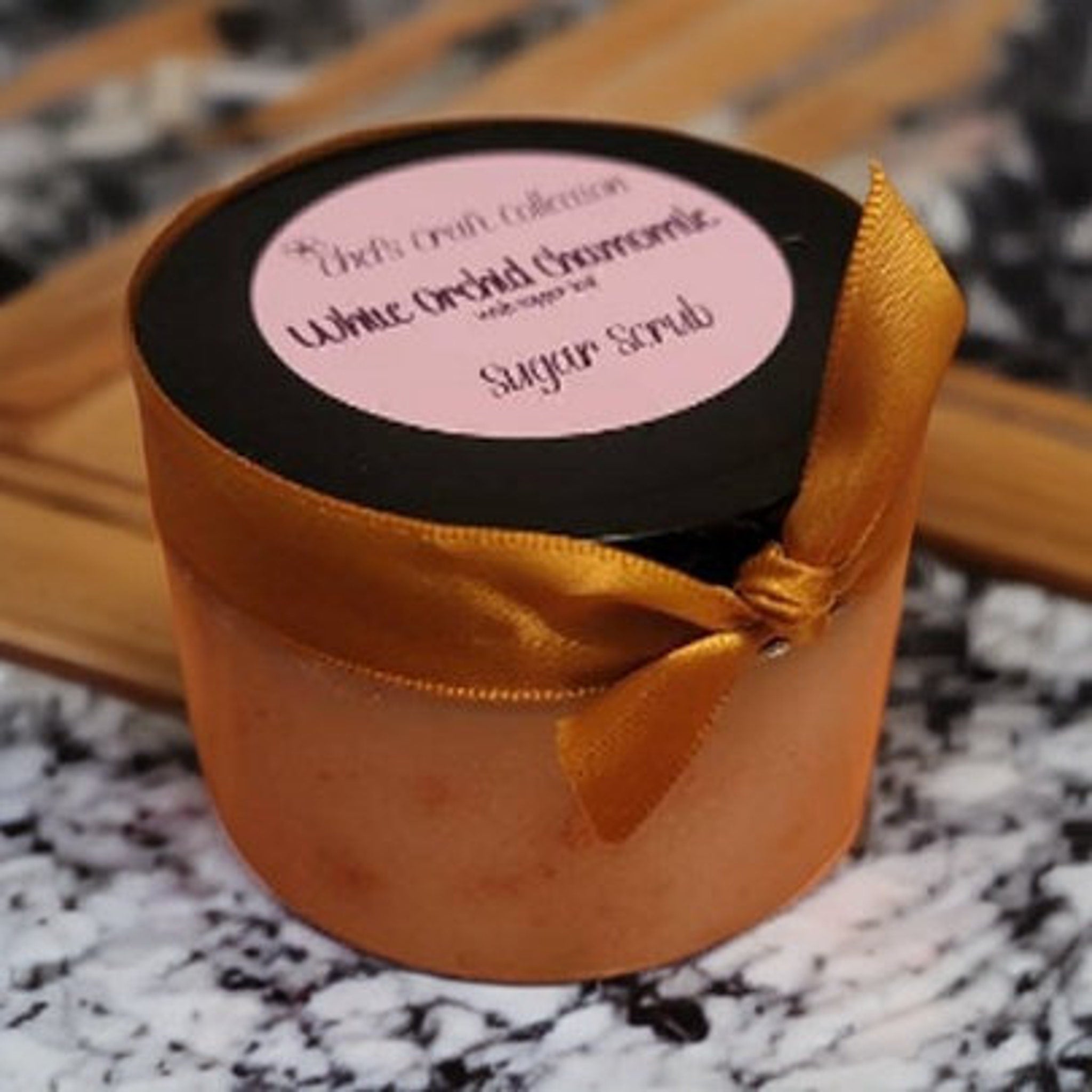 Sugar scrub jar with orange color, gold ribbon, and text label with product details