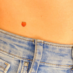 Body jewelry peach tattoo, small orange fruit design on skin, worn with denim jeans