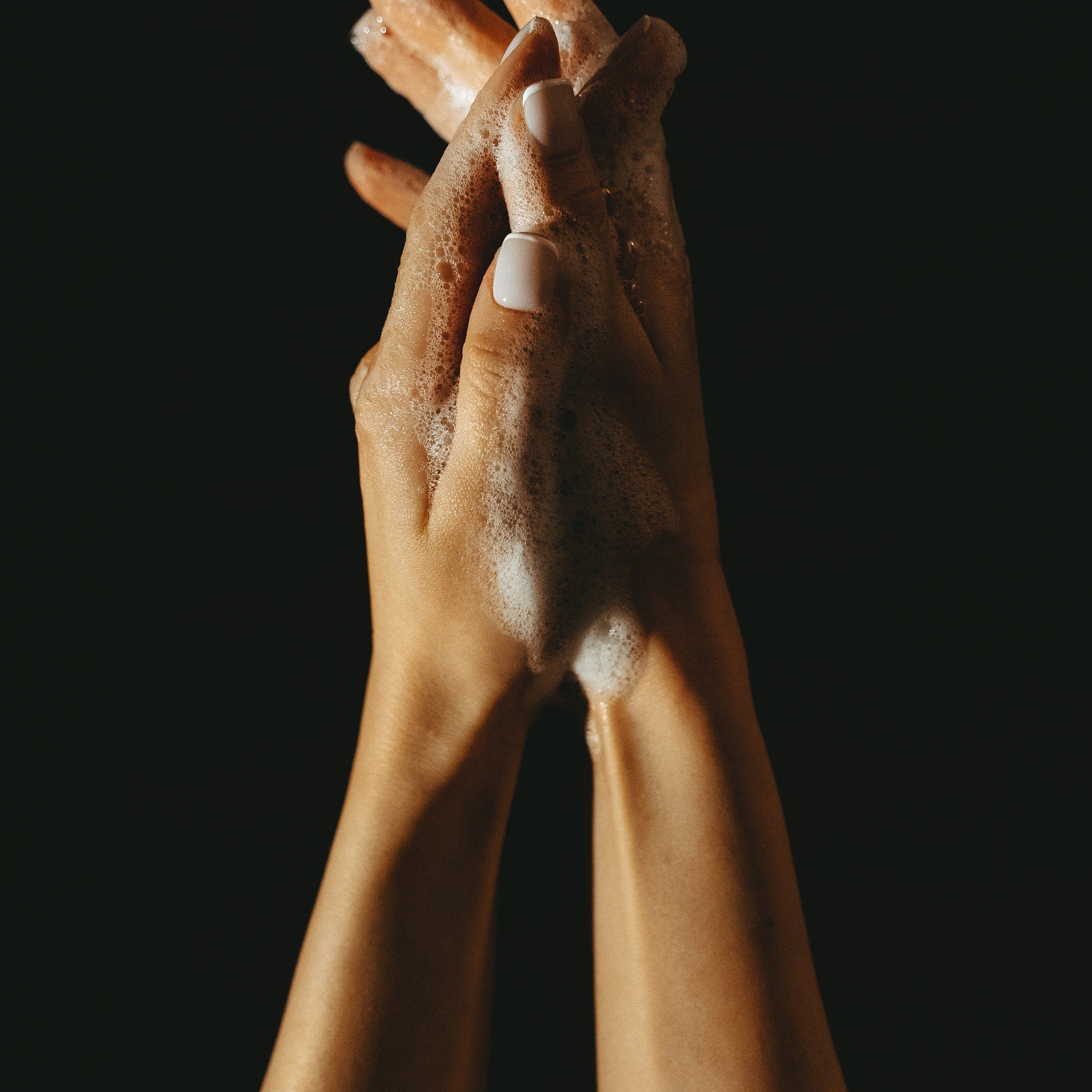Hands with white nail polish, covered in white soap bubbles against black background
